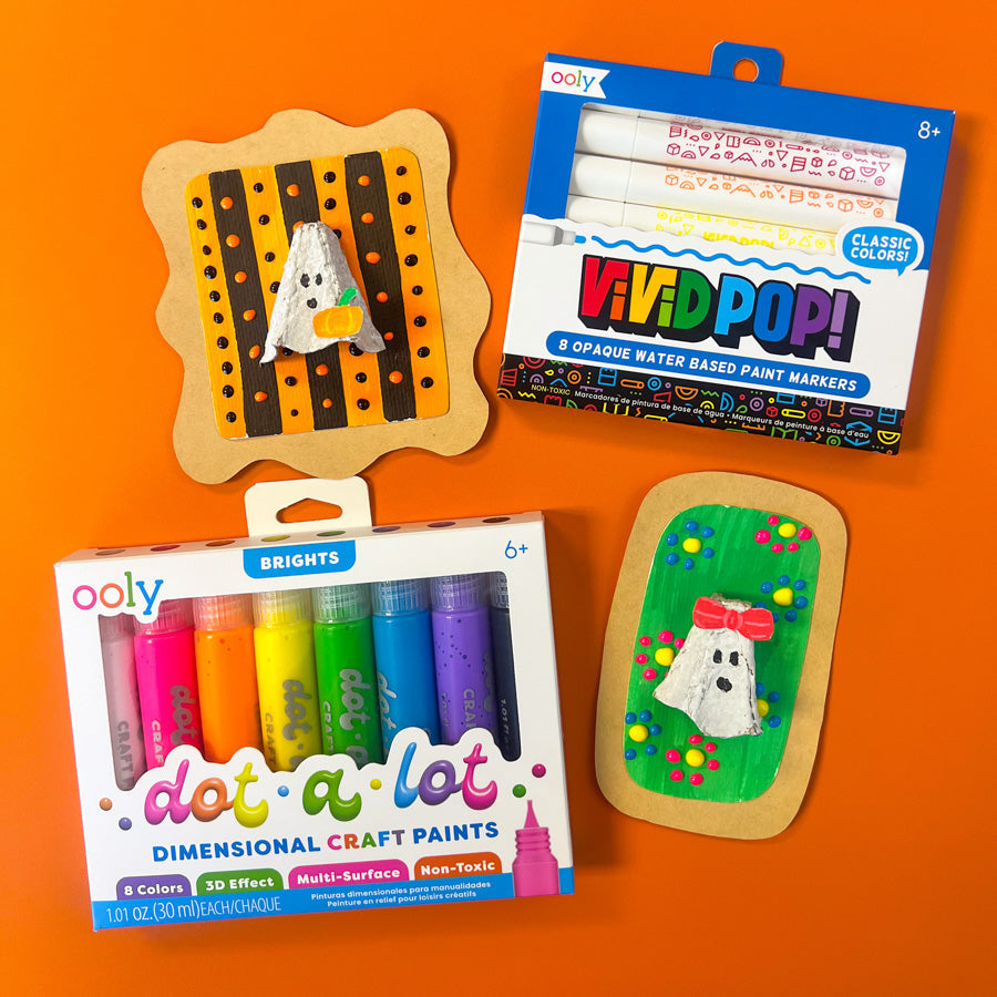 Three finished Halloween ghost crafts made from egg cartons, each decorated with colorful backgrounds and fun 3D details, displayed on an orange surface.