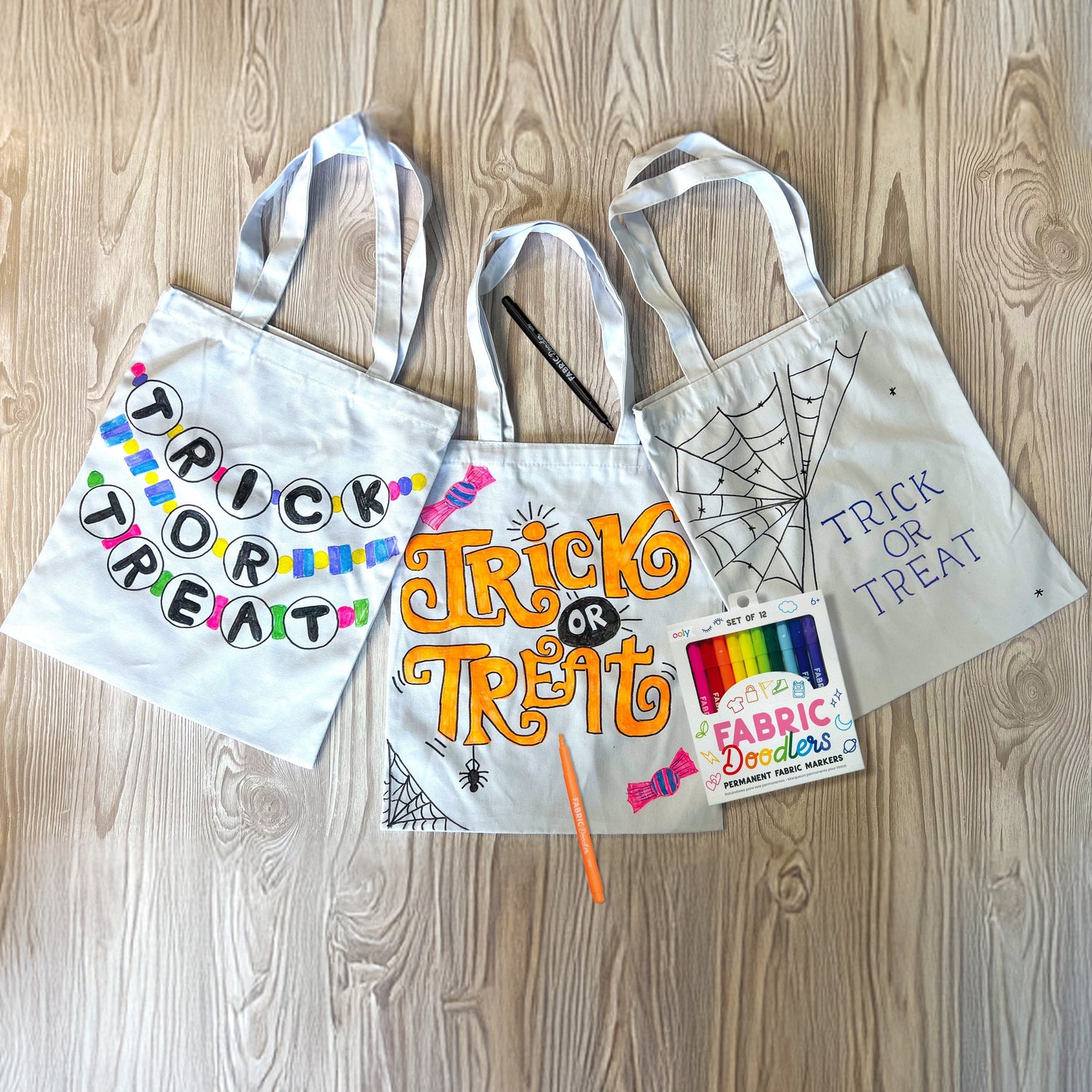 Three DIY Halloween Trick or Treat tote bags decorated with OOLY Fabric Doodlers in bracelet, candy, and spiderweb designs – OOLY Craft Blog Hero Image.