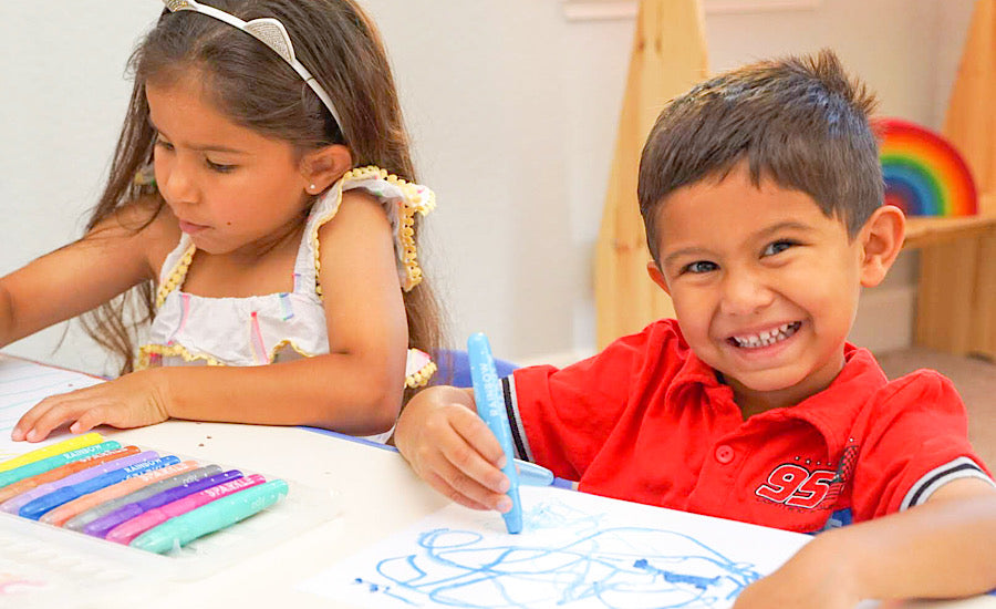 two children sitting at white table coloring with watercolor crayons