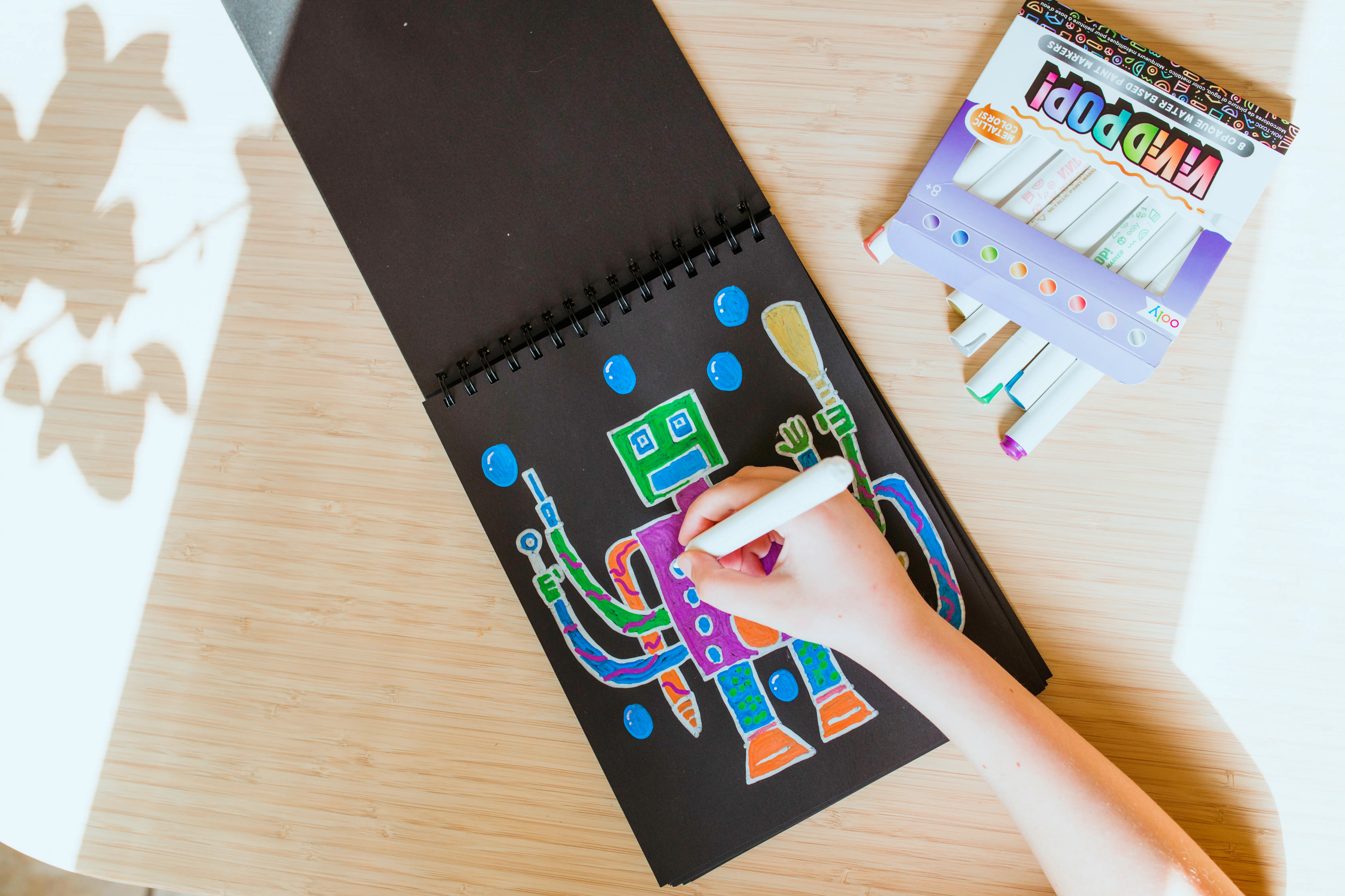 Kid coloring drawing of robot on black paper with OOLY Vivid Pop! Metallic Paint Markers