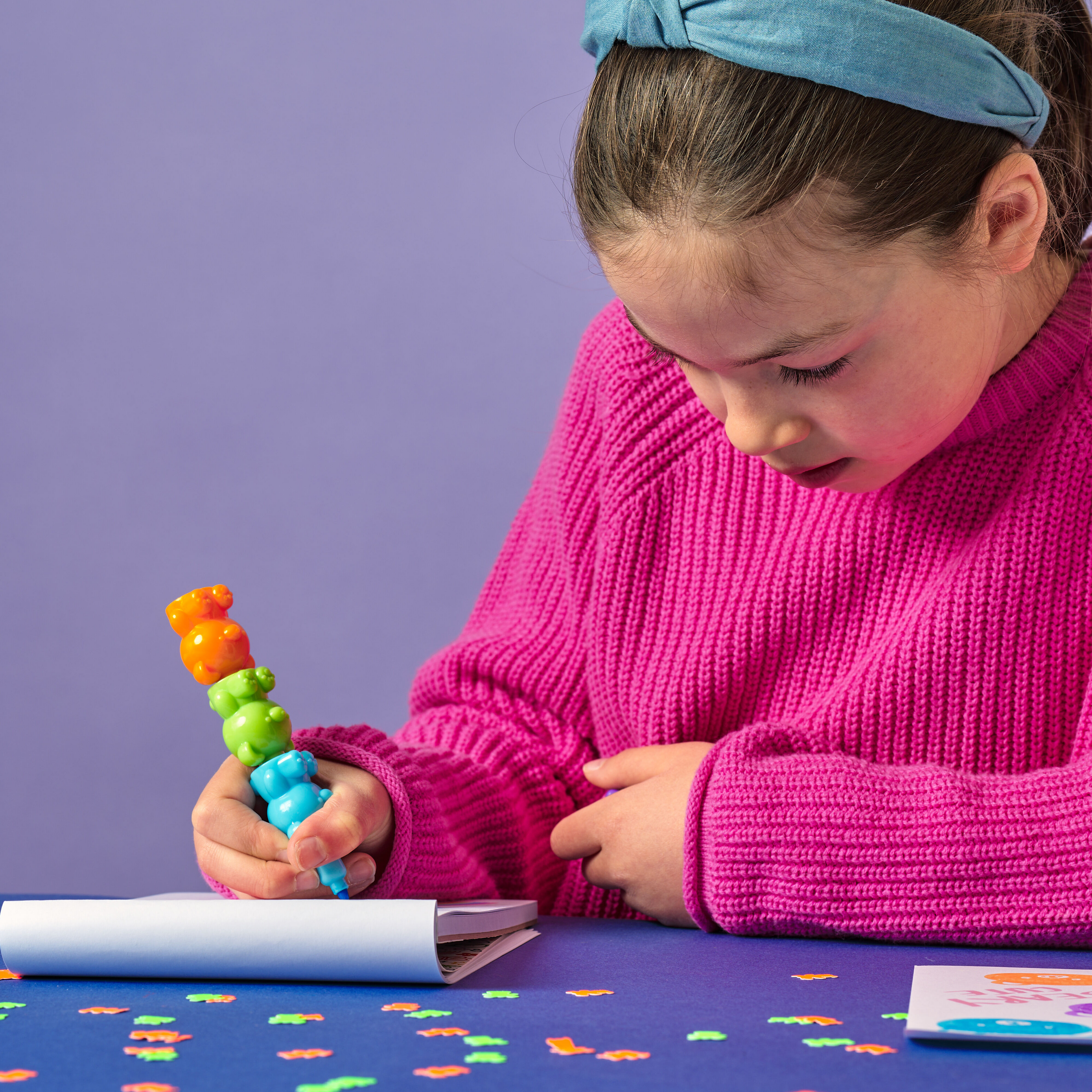 Girl drawing in a white sketchbook with OOLY Bear Besties Stacking Highlighters on a blue table