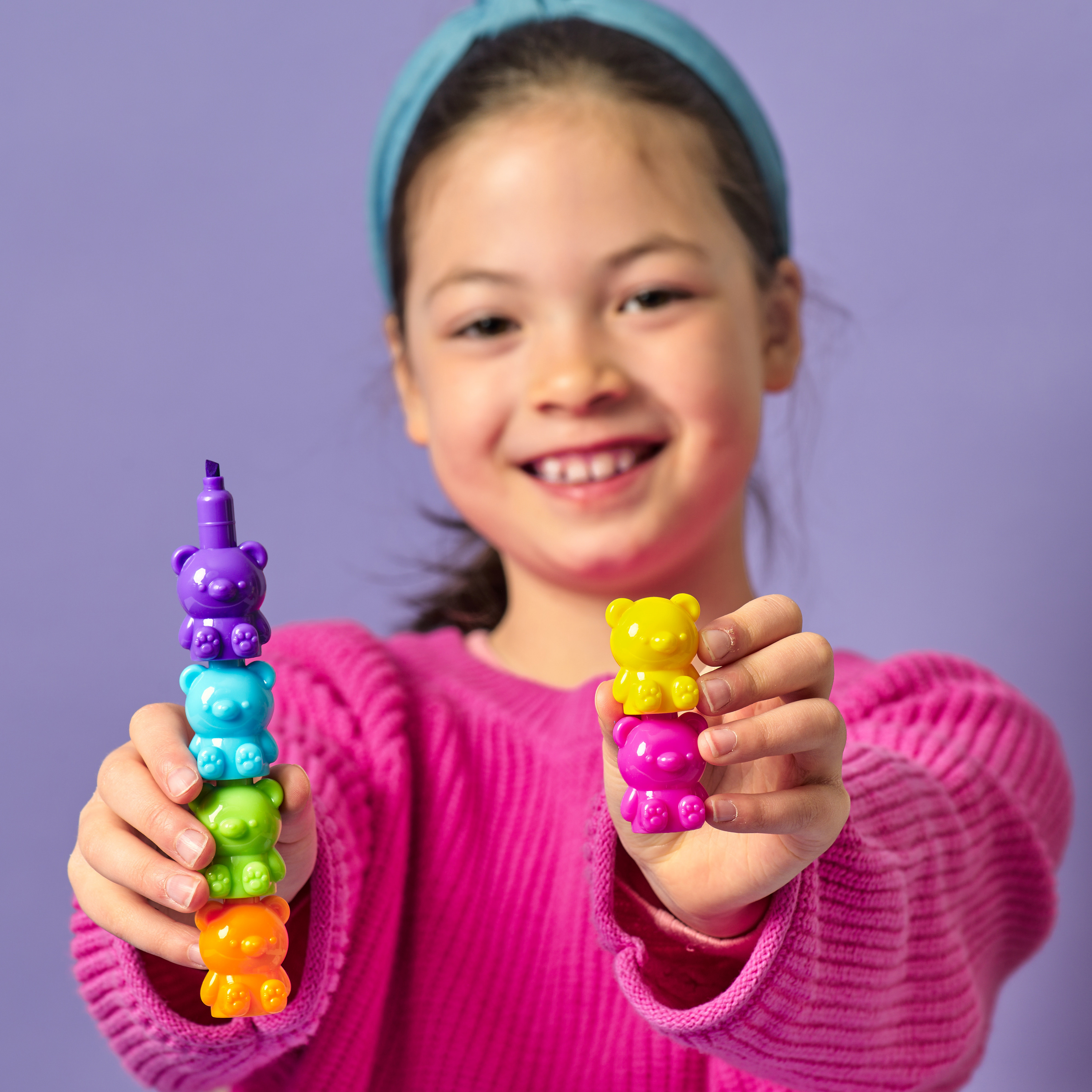 Girl holding OOLY Bear Besties Stacking Highlighters in two different pieces on a purple background