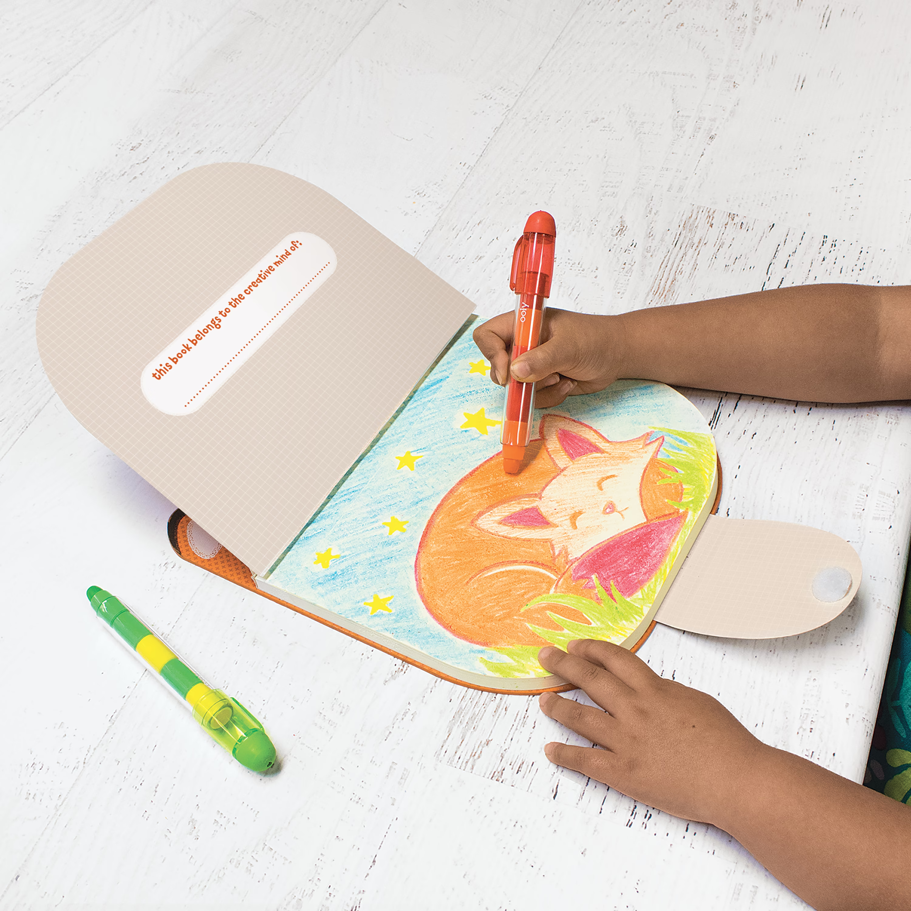 Kid coloring in a fox in OOLY Carry Along Sketchbook on white wooden table