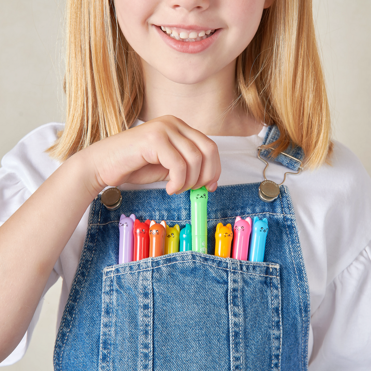 Close up of girl with collection of OOLY Cat Parade Gel Crayons in her overalls pocket