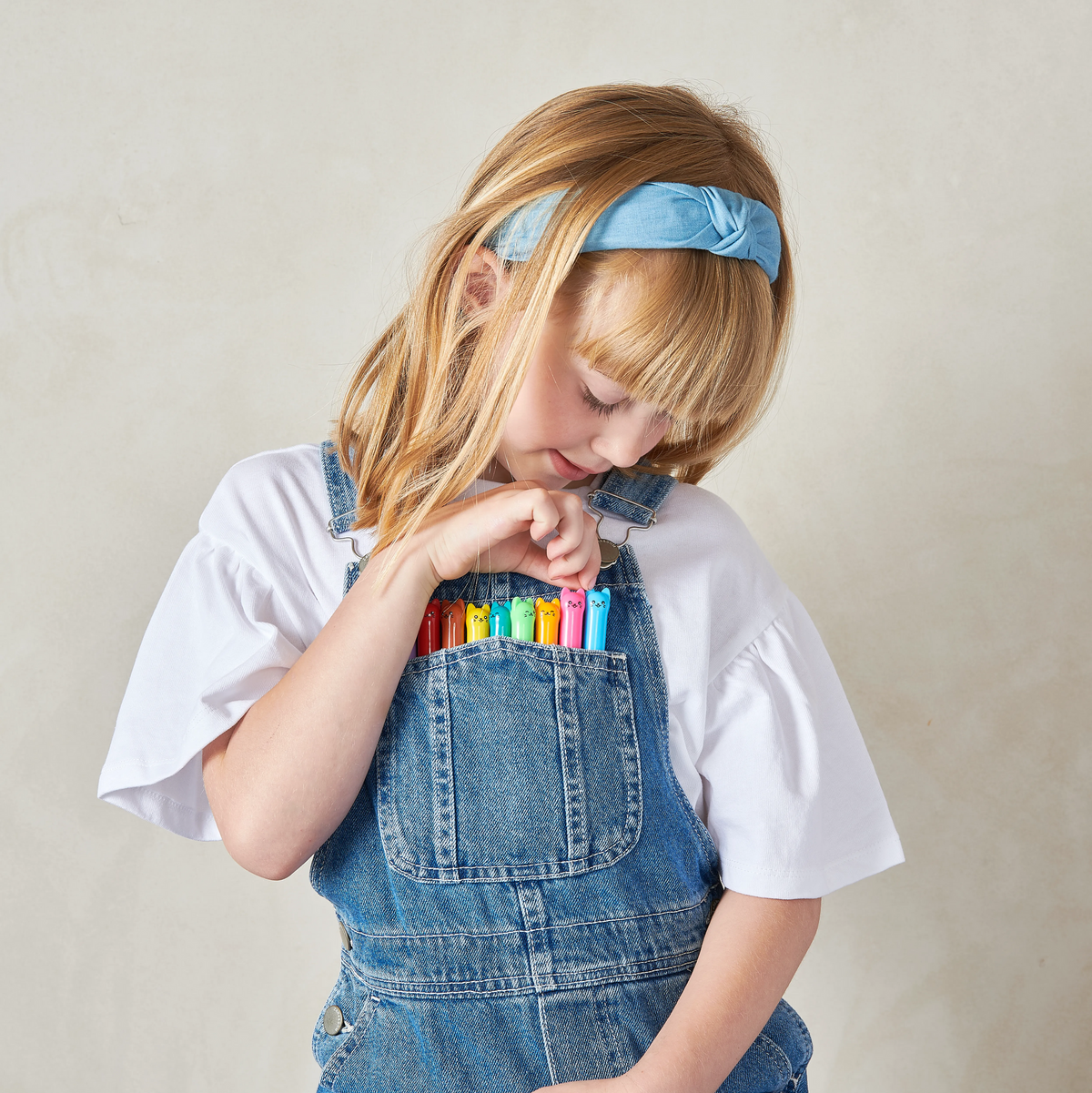 Girl with collection of OOLY Cat Parade Gel Crayons in her overalls pocket