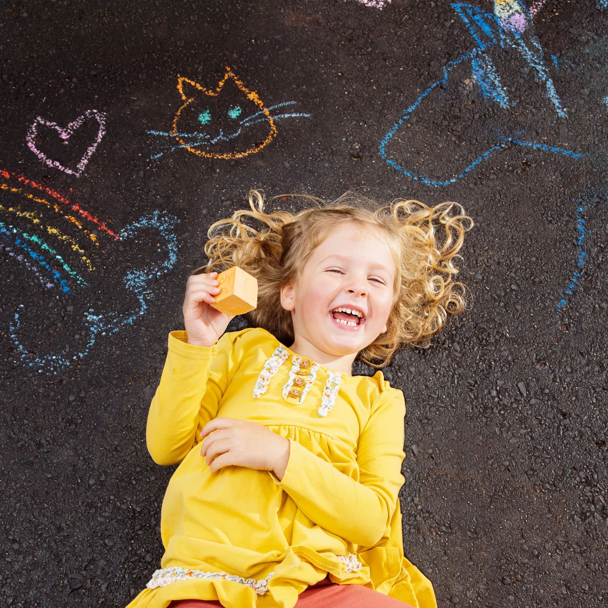 Girl laughing and laying on ground with chalk drawings made with OOLY Chalk-O-Rama Block Sidewalk Chalk