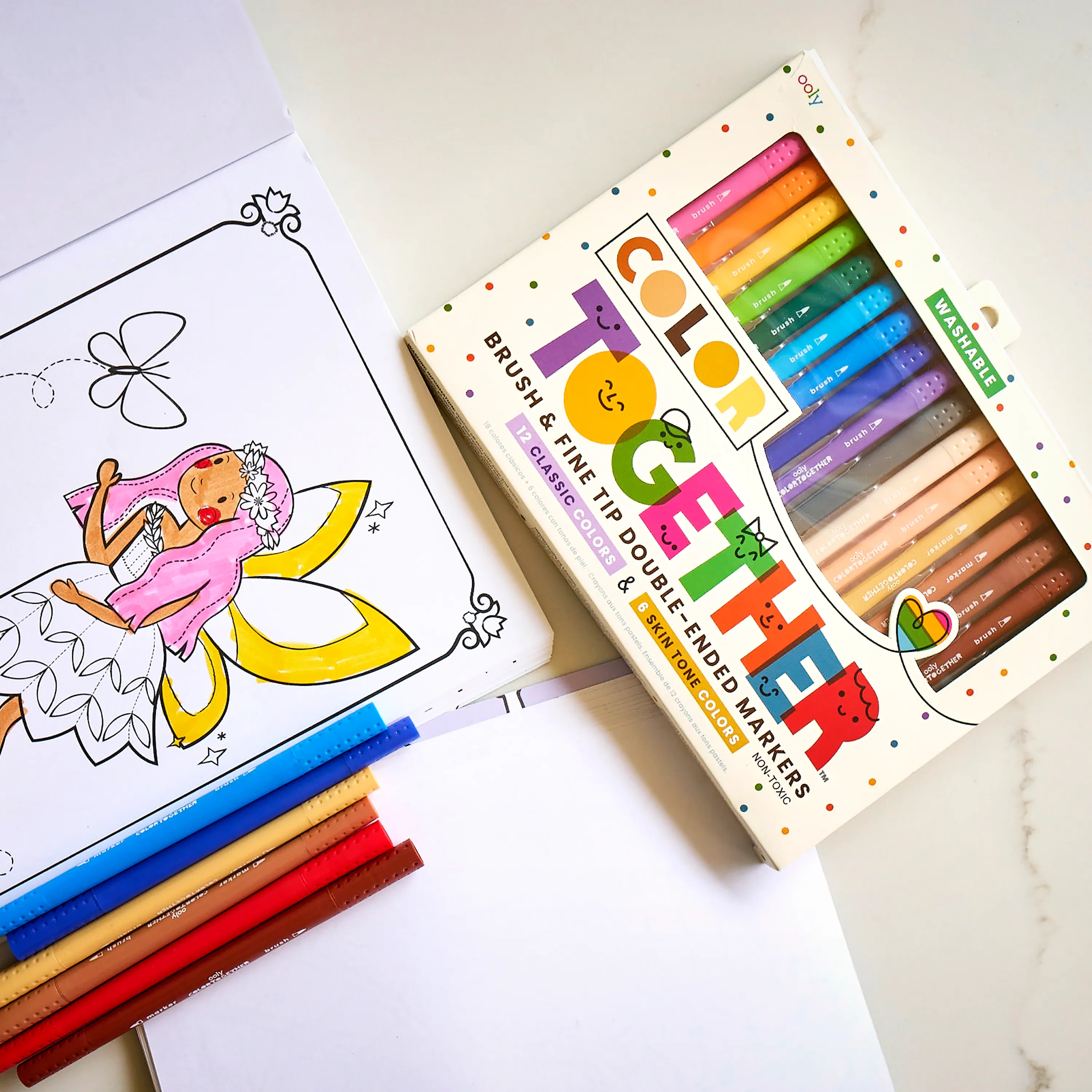 Fairy coloring page and set of OOLY Color Together double ended markers on a desktop