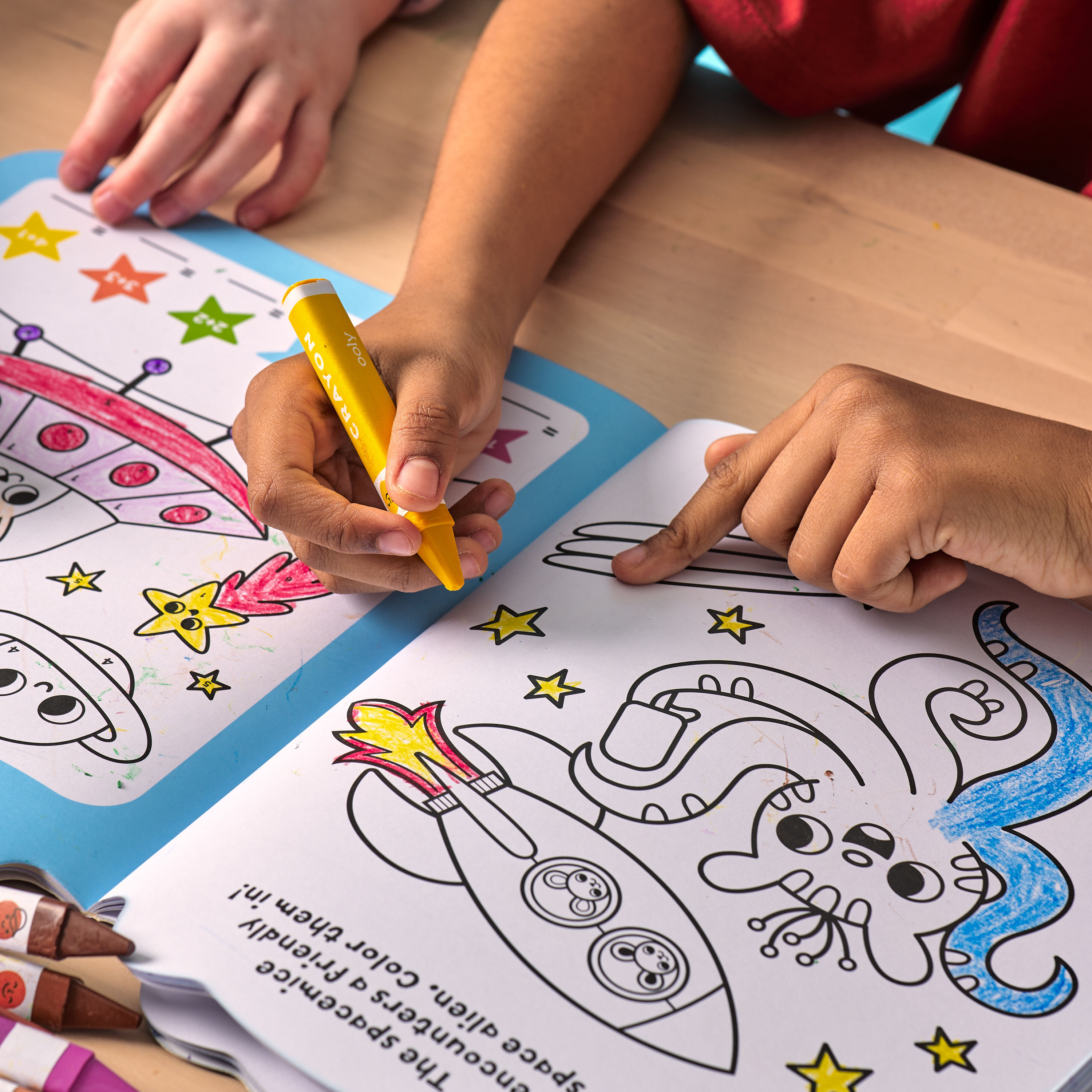 Kid coloring stars in an activity book with a yellow OOLY Color Together Triangular Crayon