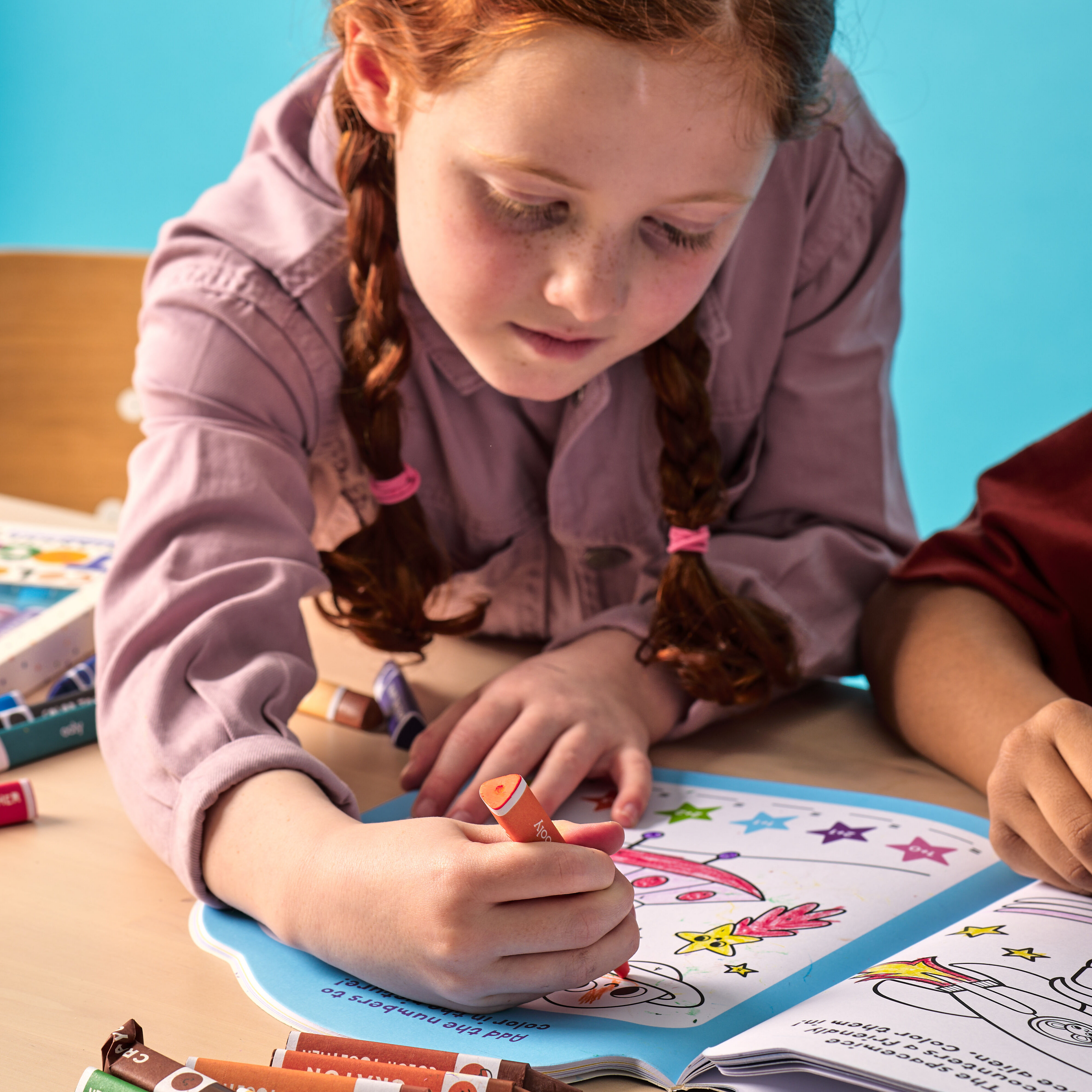 Girl coloring in activity book with an orange OOLY Color Together Triangular Crayon