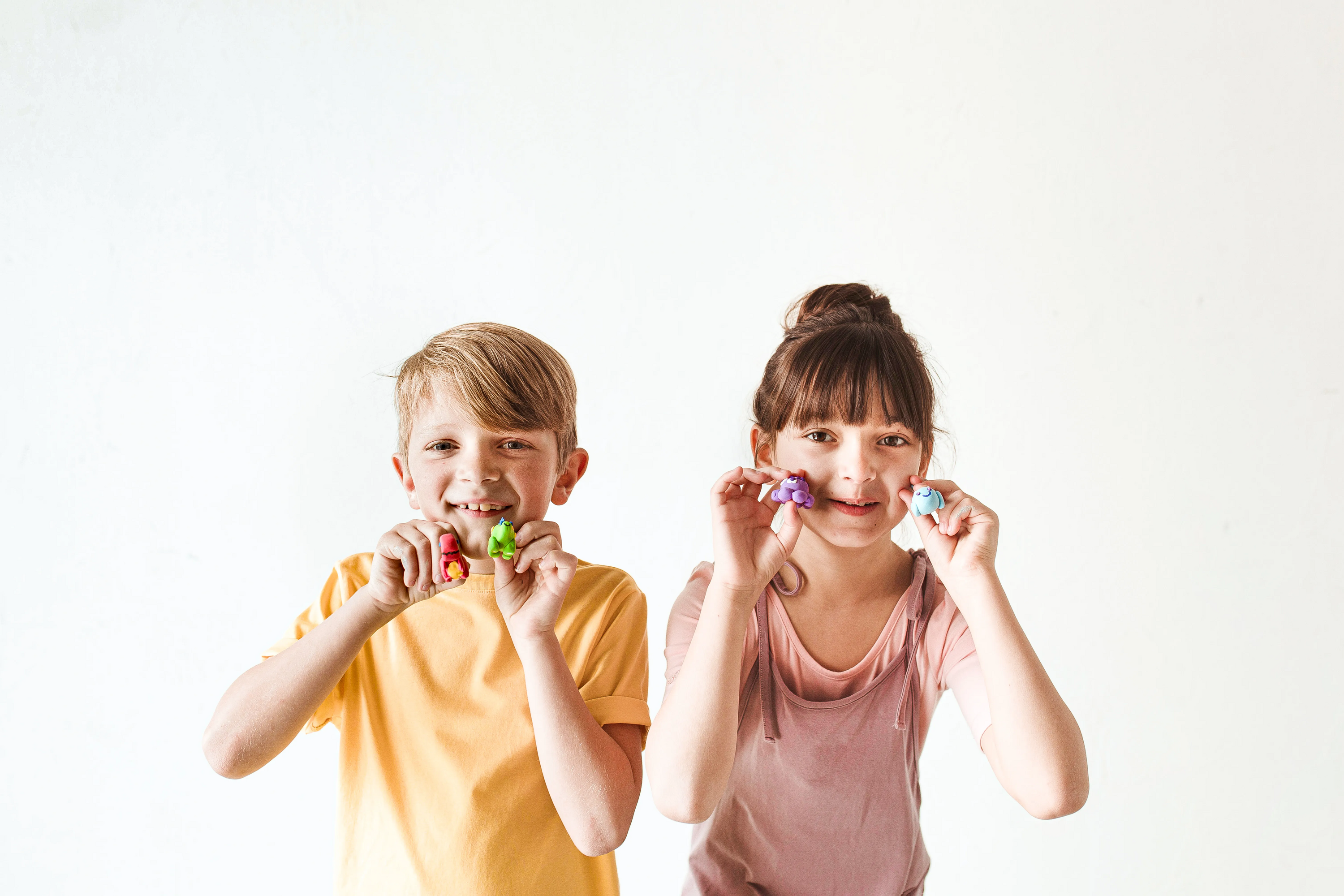 Boy and girl holding up finished clay animals from OOLY Creatibles Mini Air Dry Clay Kits