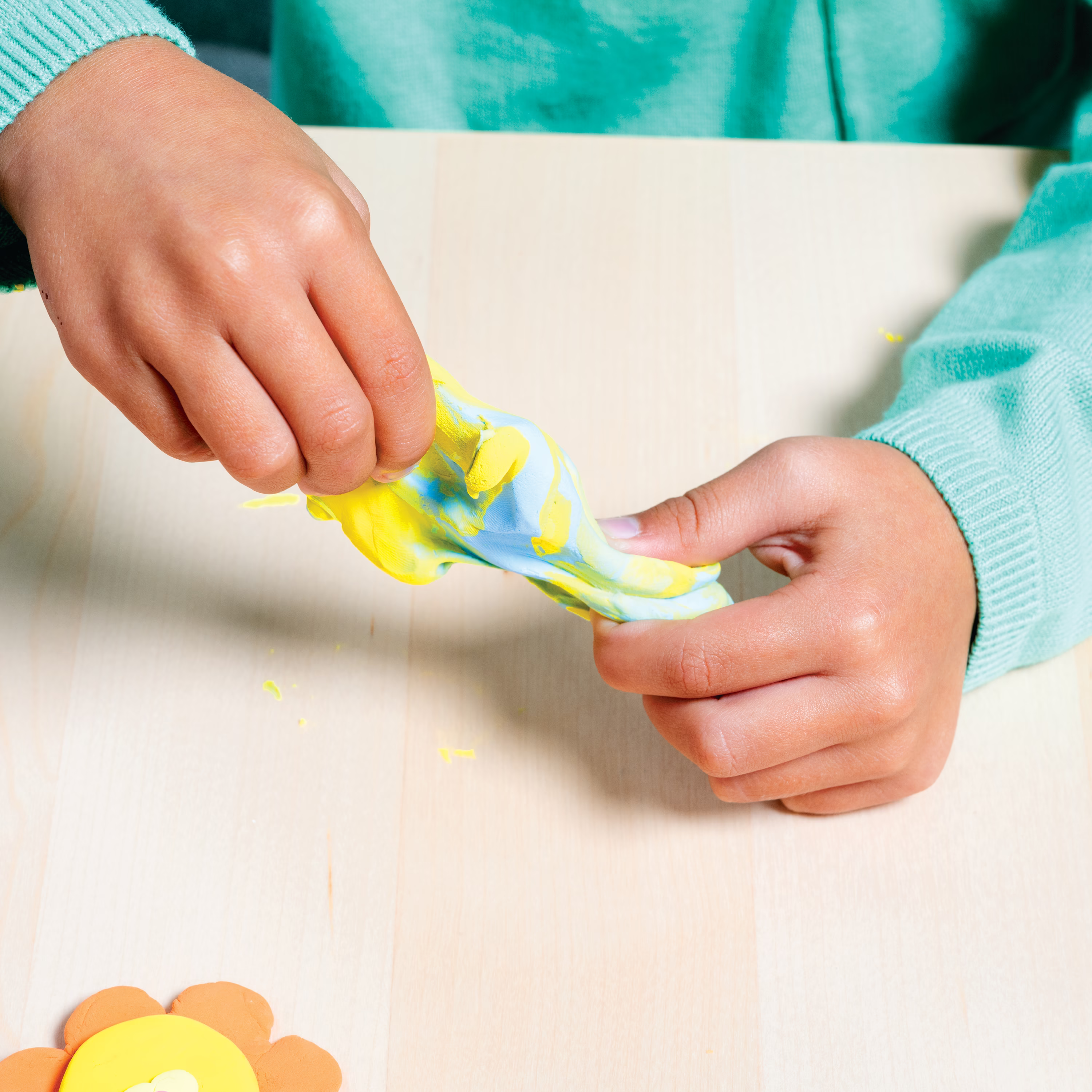 Kid combining blue and yellow clay from OOLY Creatibles Deluxe Air Dry Clay Kit