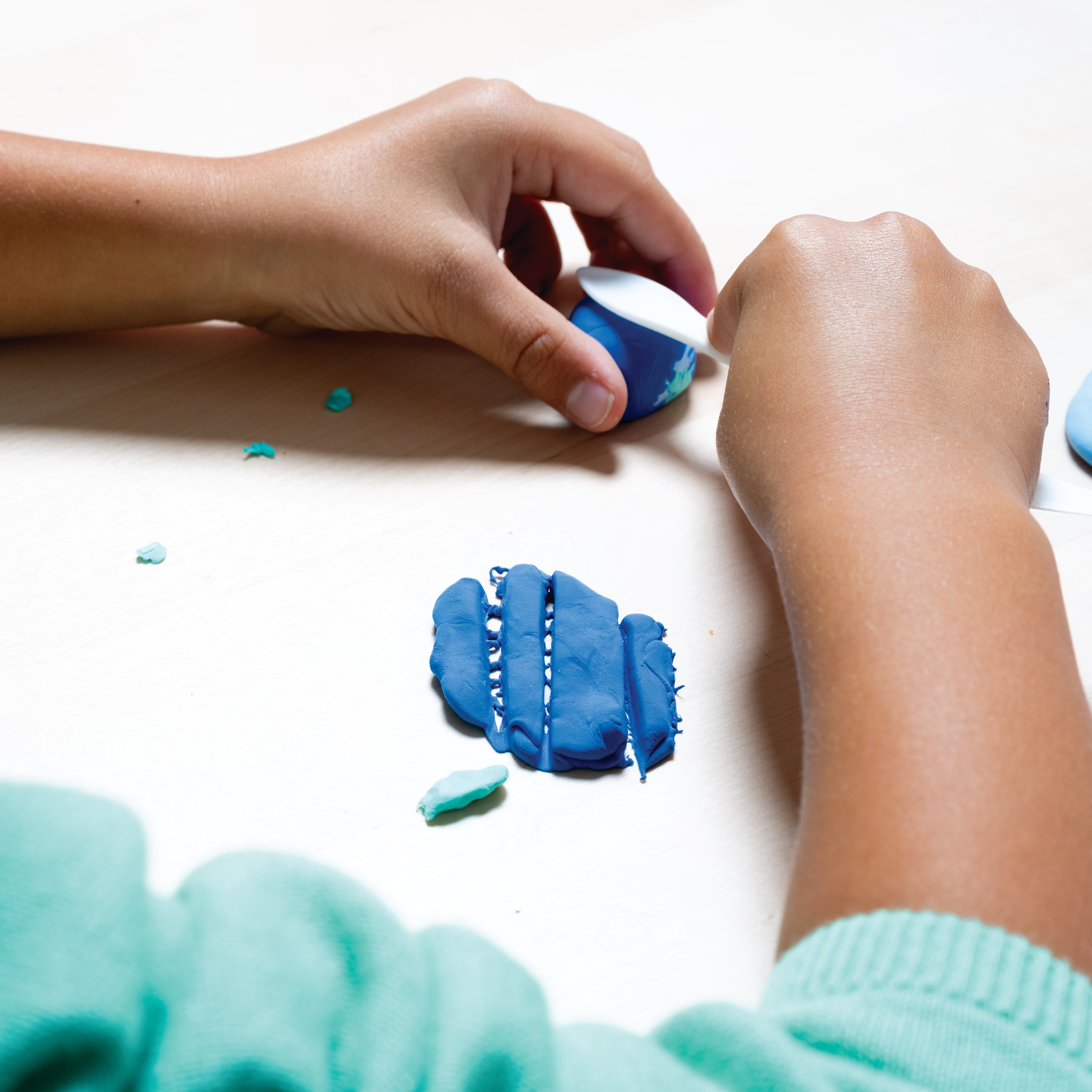 Kid shaping blue clay with clay shaping tool from OOLY Creatibles Deluxe Air Dry Clay Kit