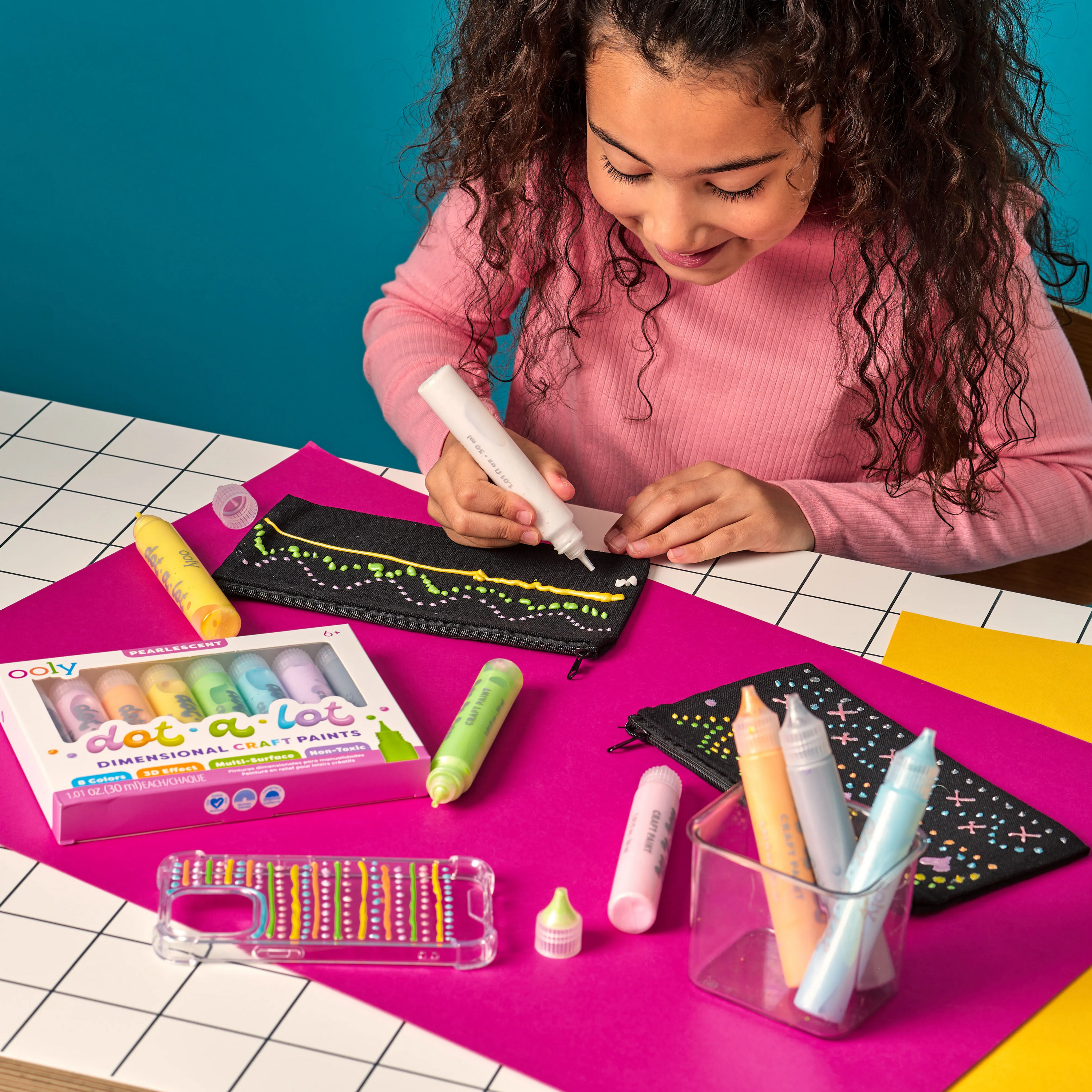 Girl using OOLY Dot-a-Lot 3D Dimensional Craft Paint on a pink mat with colorful paint sticks.