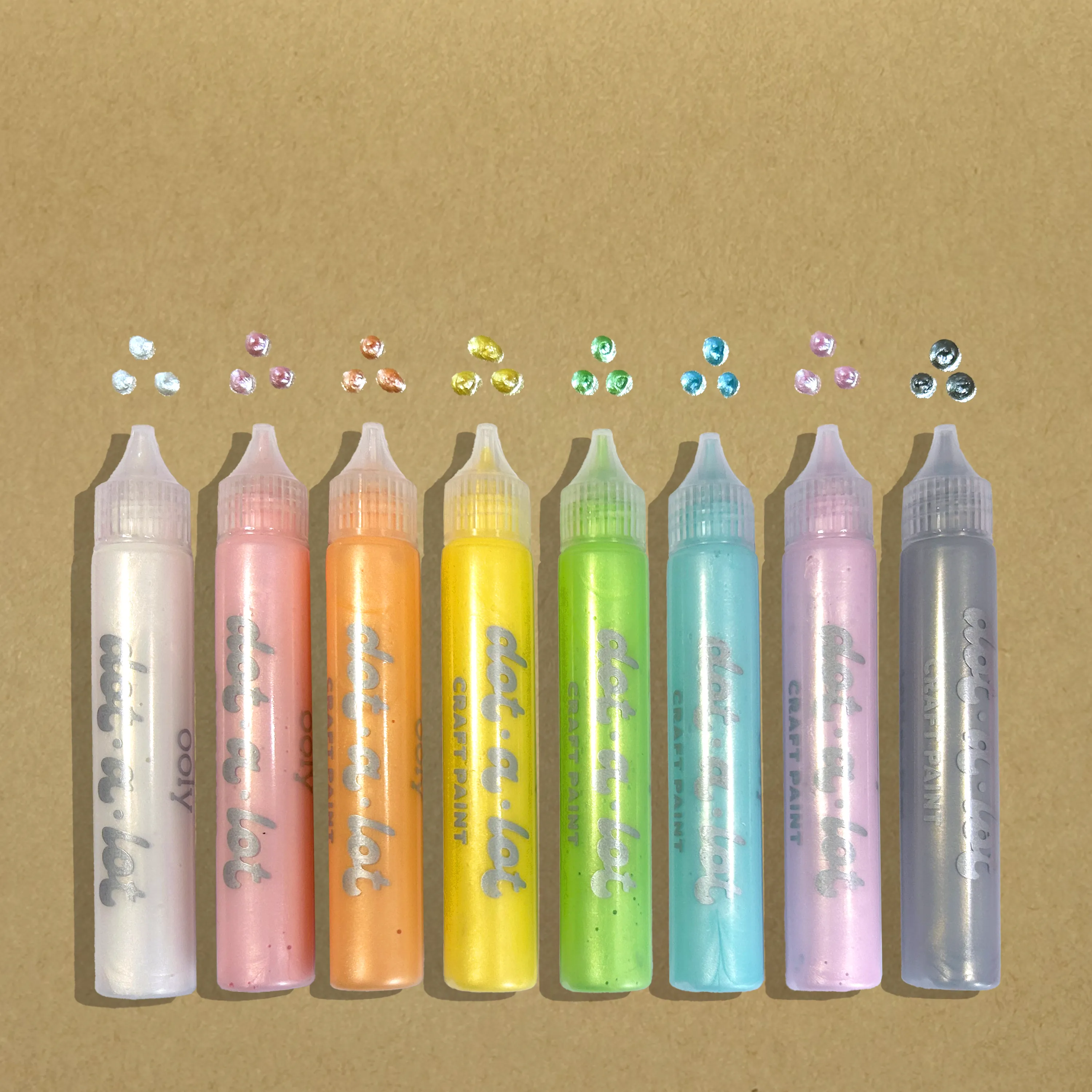 Row of eight colored sticks of OOLY Dot-a-Lot 3D Dimensional Craft Paint - Pearlescent a kraft paper background