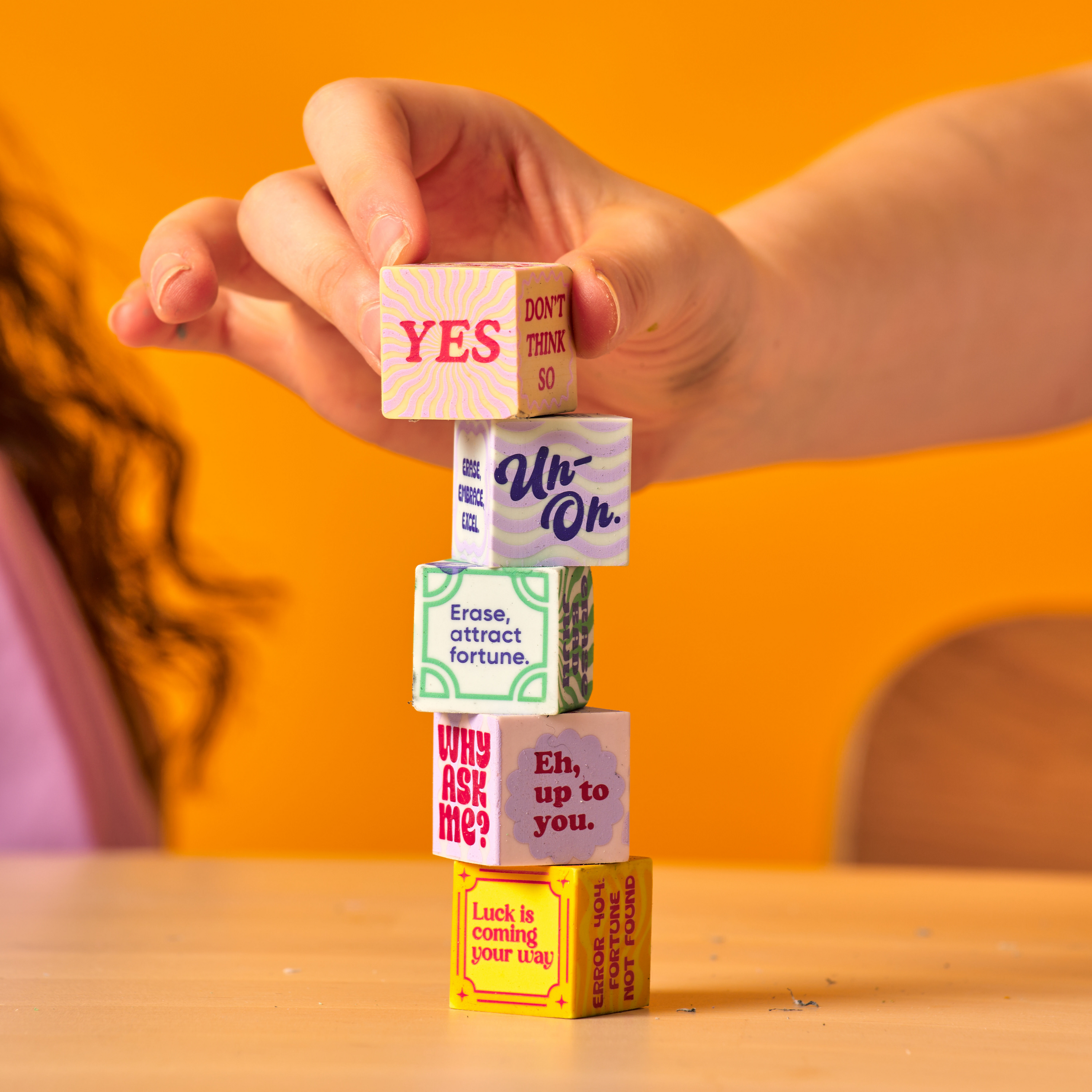 Hand stacking all five OOLY Feeling Lucky Dice Erasers on a table