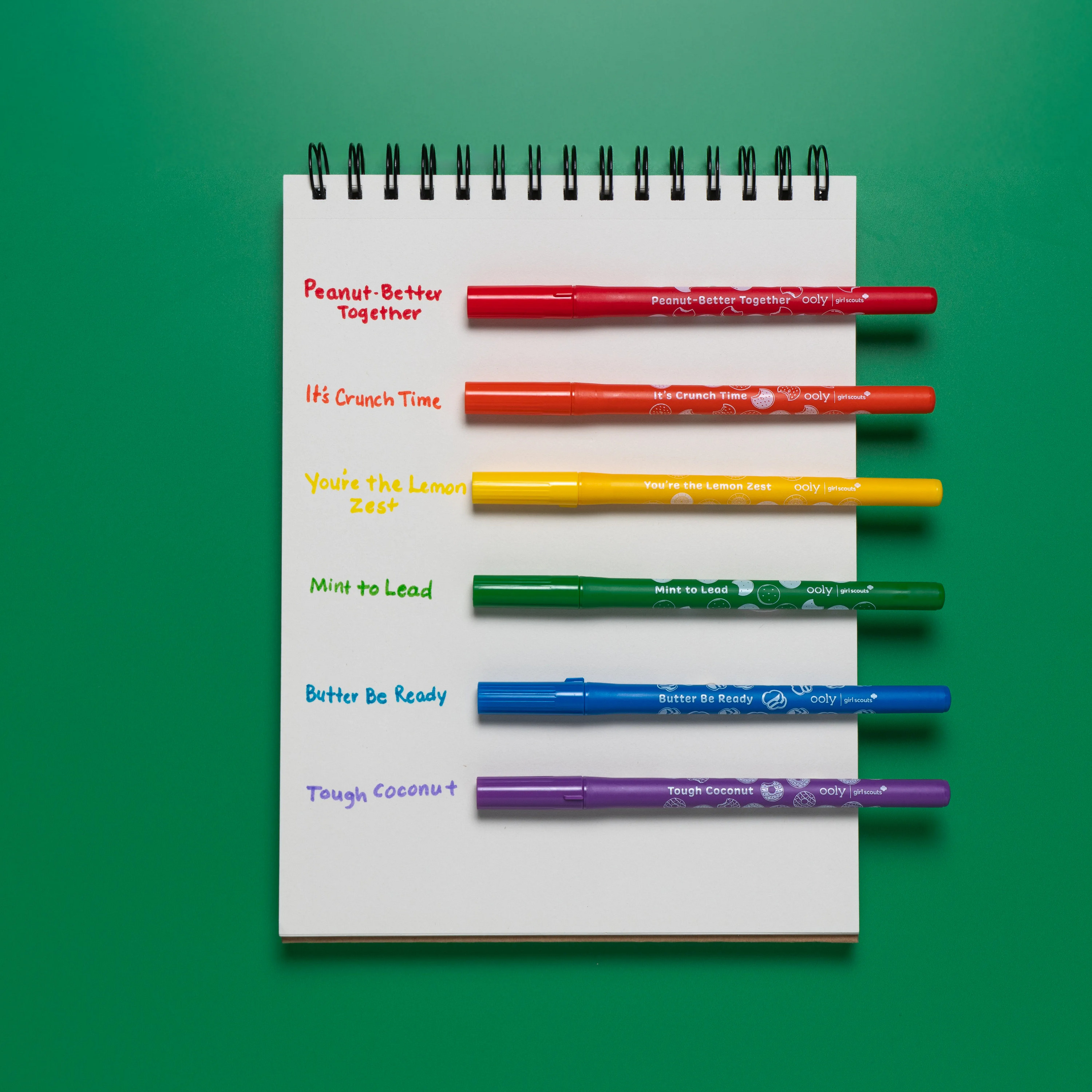 Sketchbook with OOLY x Girl Scouts Cookie Scented Markers resting next to handwritten scent names as swatches