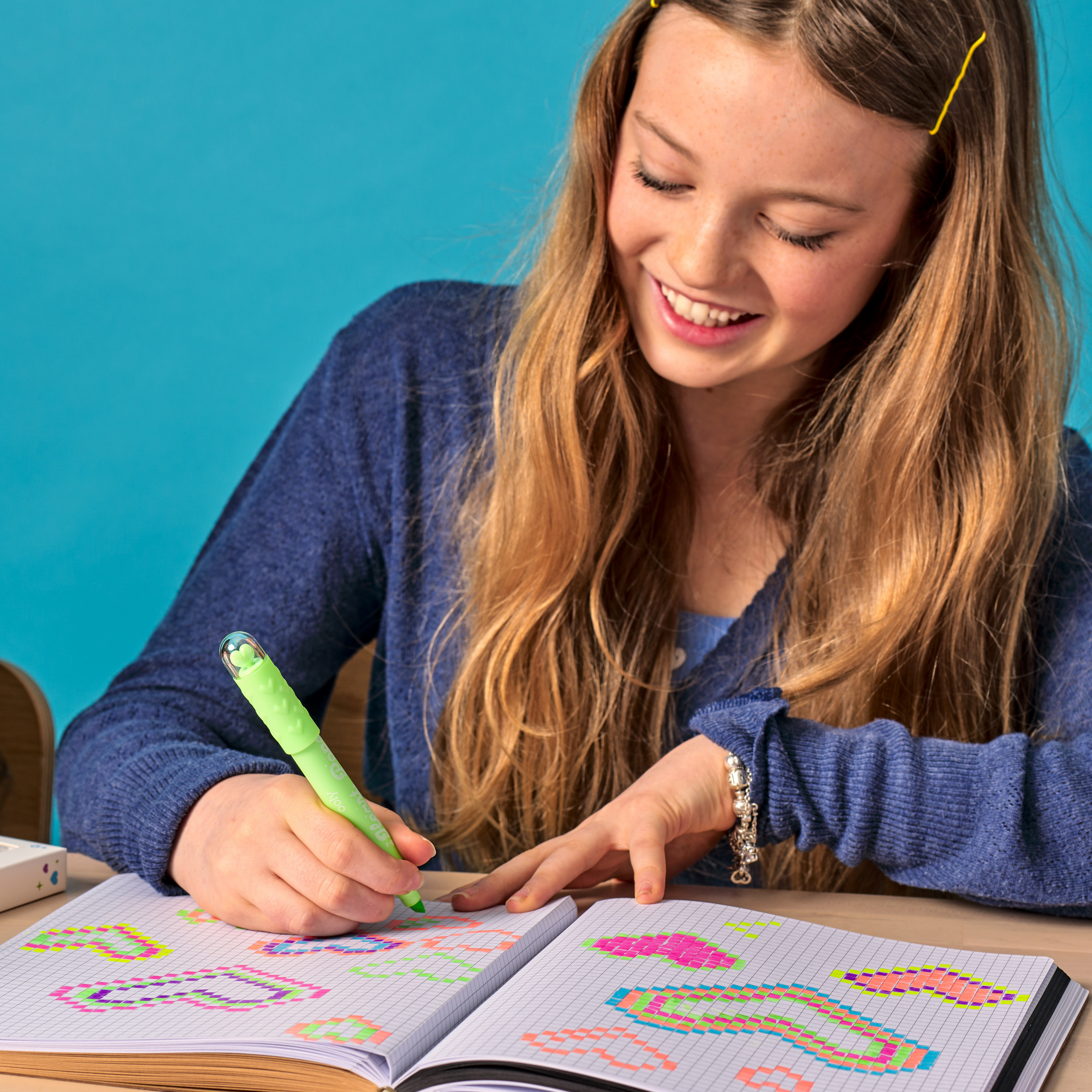 Girl making heart pixel art on a graph paper book using a green OOLY Heart Pops Neon Highlighter