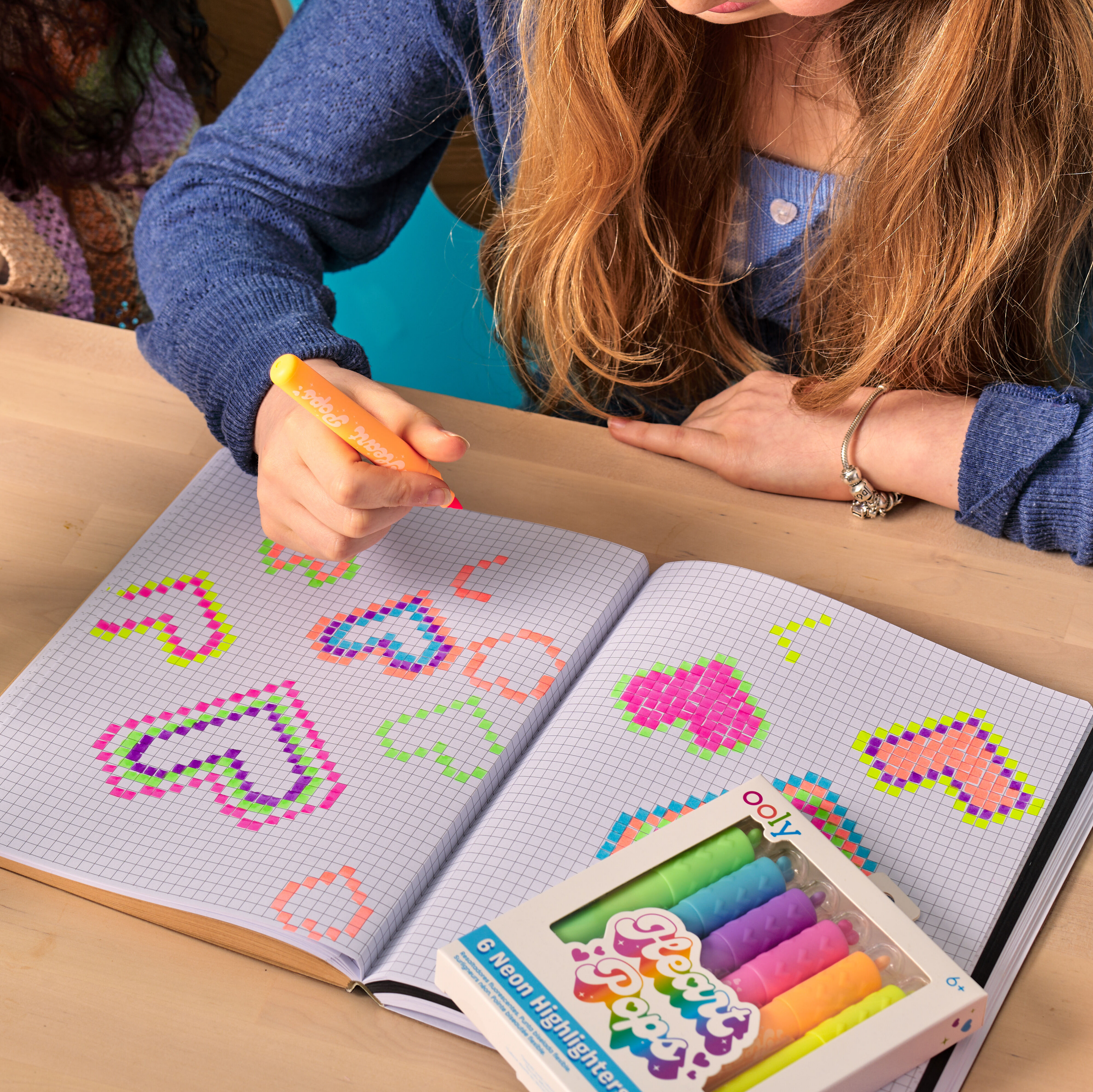 Girl making heart pixel art on graph paper with a set of OOLY Heart Pops Neon Highlighters