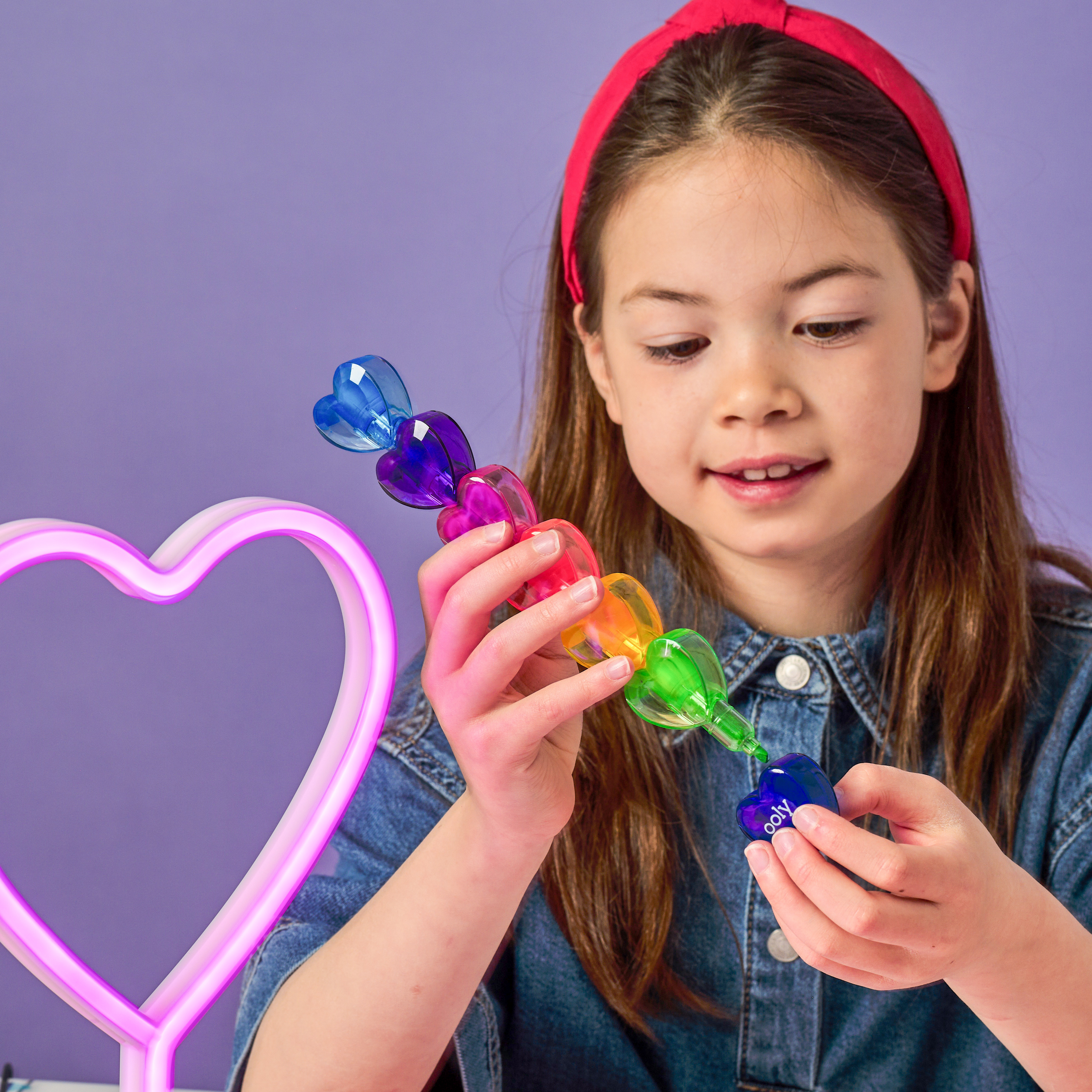Girl connecting OOLY Heart Stacks Stacking Highlighters on a purple background