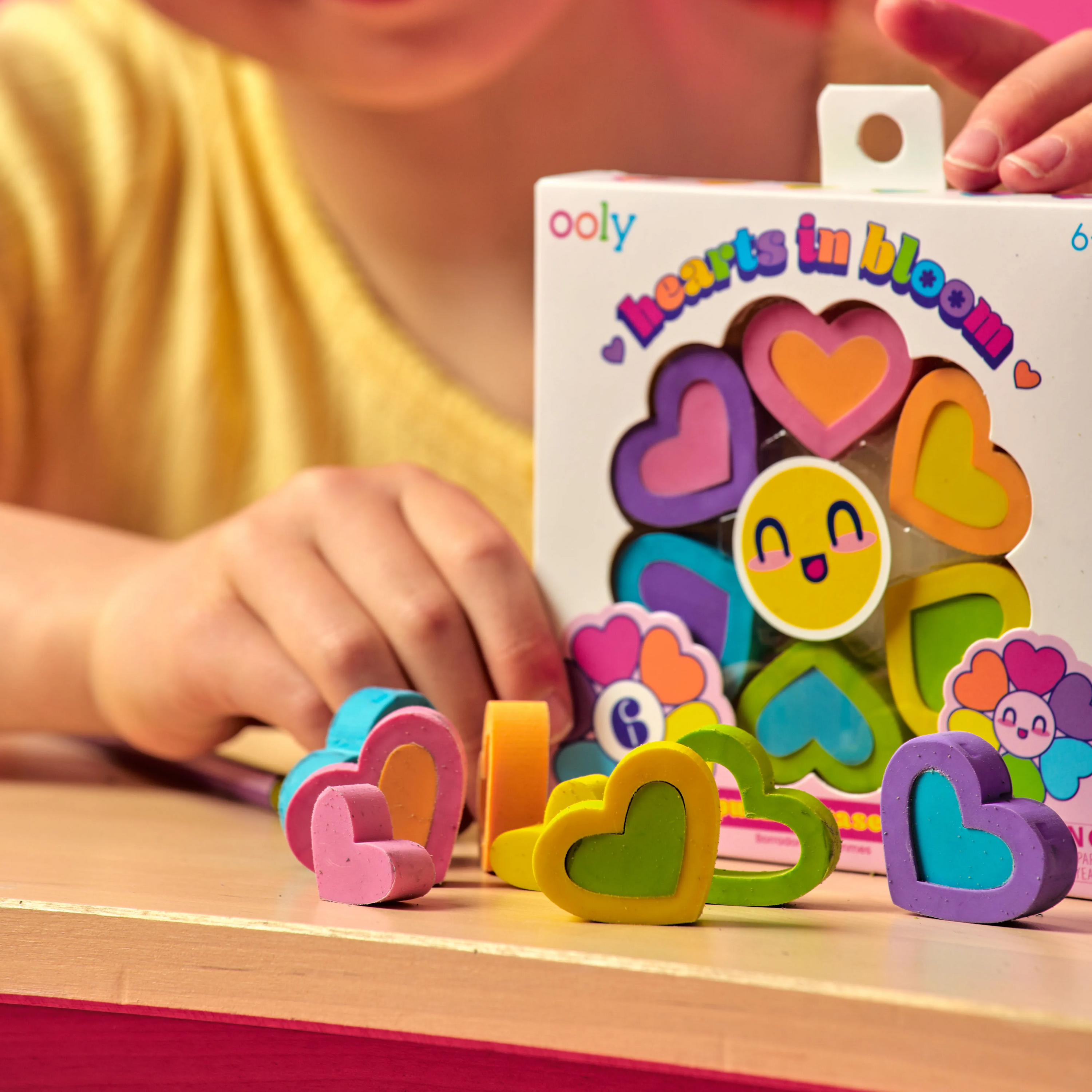 Girl holding a set of OOLY Hearts in Bloom Puzzle Erasers with heart erasers out on a wooden table