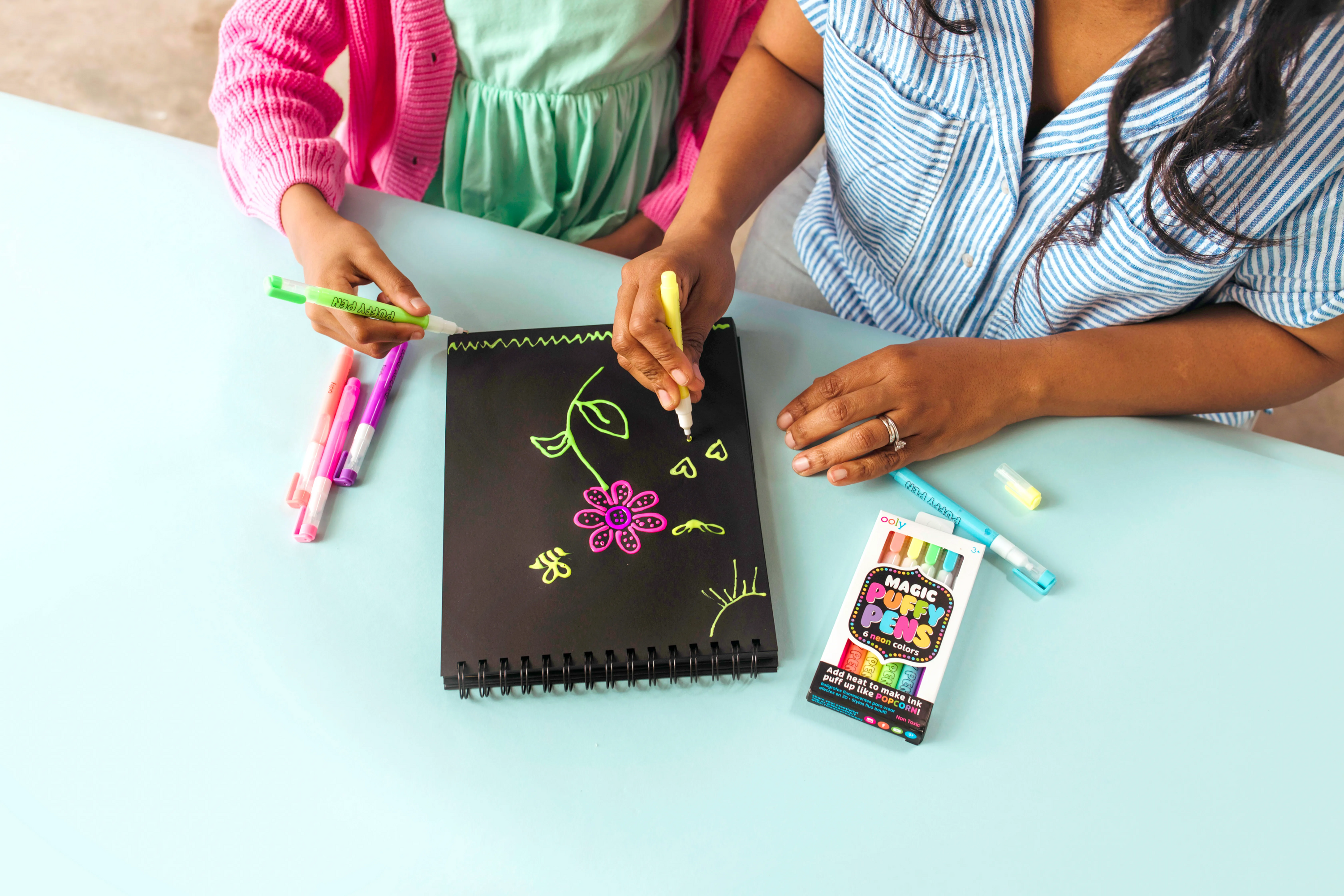 Couple coloring with OOLY Magic Puffy Neon Pens on black paper pad medium shot