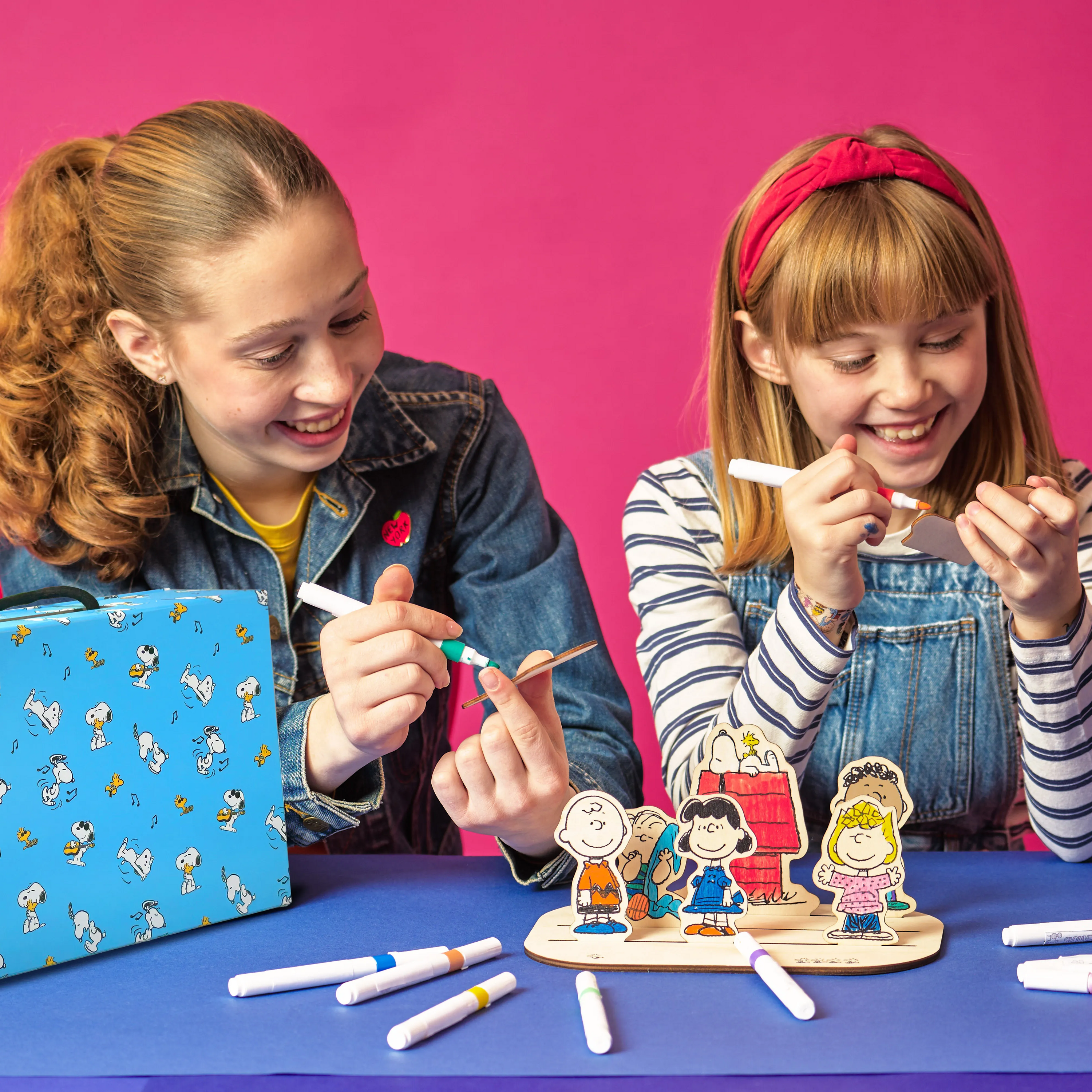 Two people coloring wood pieces with markers from the OOLY x Peanuts Color-In Wooden Scene Kit