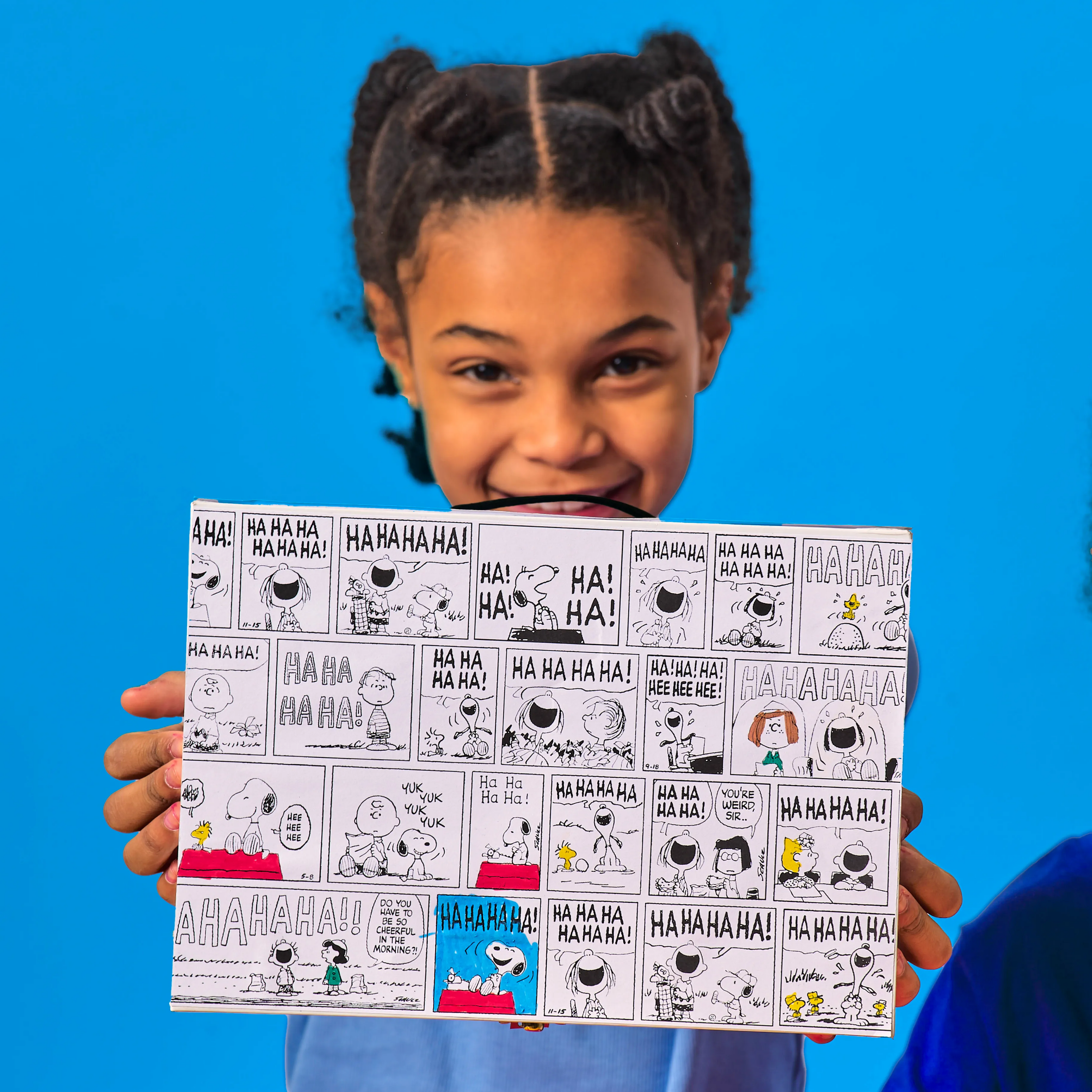 Girl holding up colored box from an OOLY x Peanuts Coloring Activity & Sticker Kit