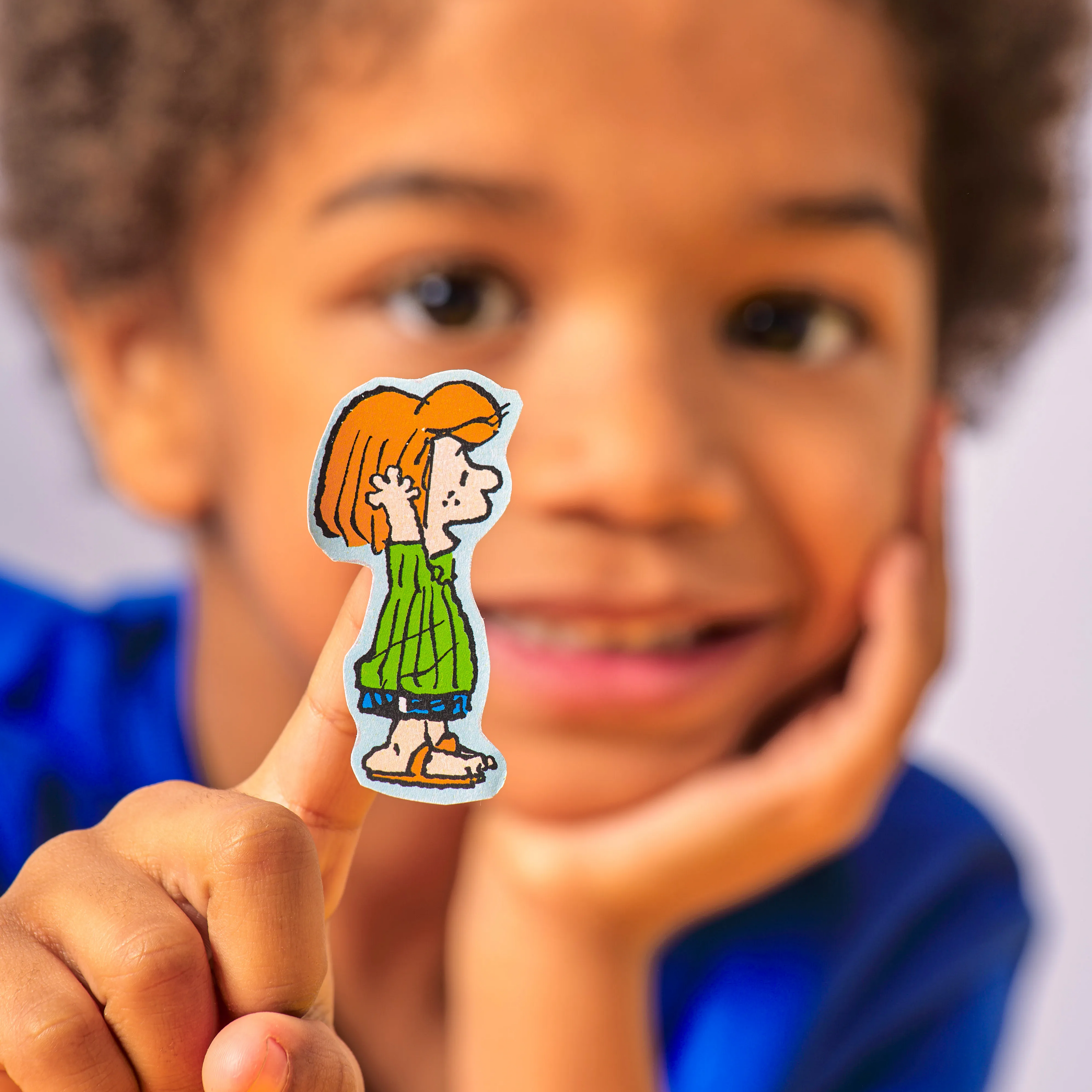 Kid holding up sticker of Peppermint Patty from the OOLY x Peanuts Coloring Activity & Sticker Kit