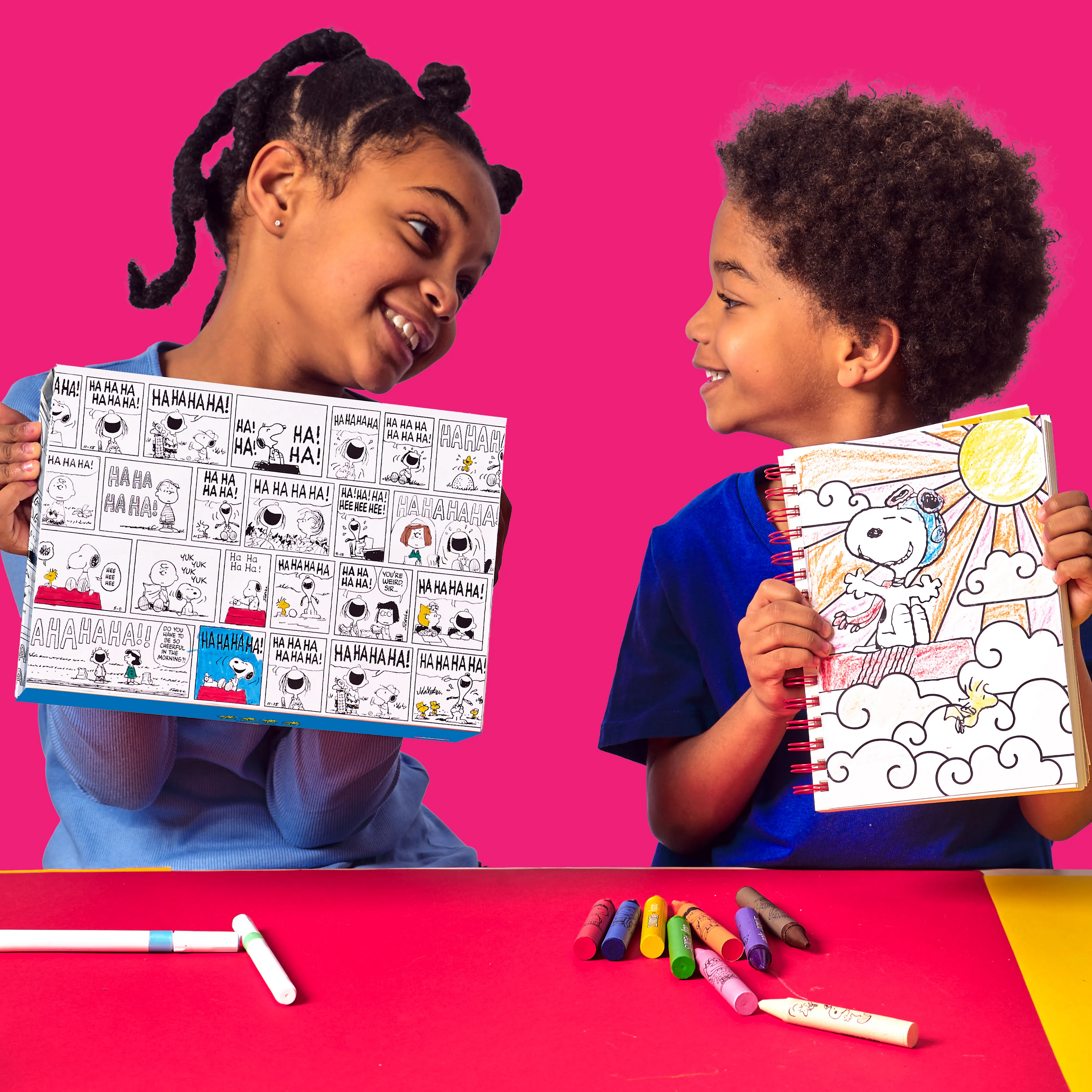 Two kids holding up Peanuts activity projects from the OOLY x Peanuts Coloring Activity & Sticker Kit