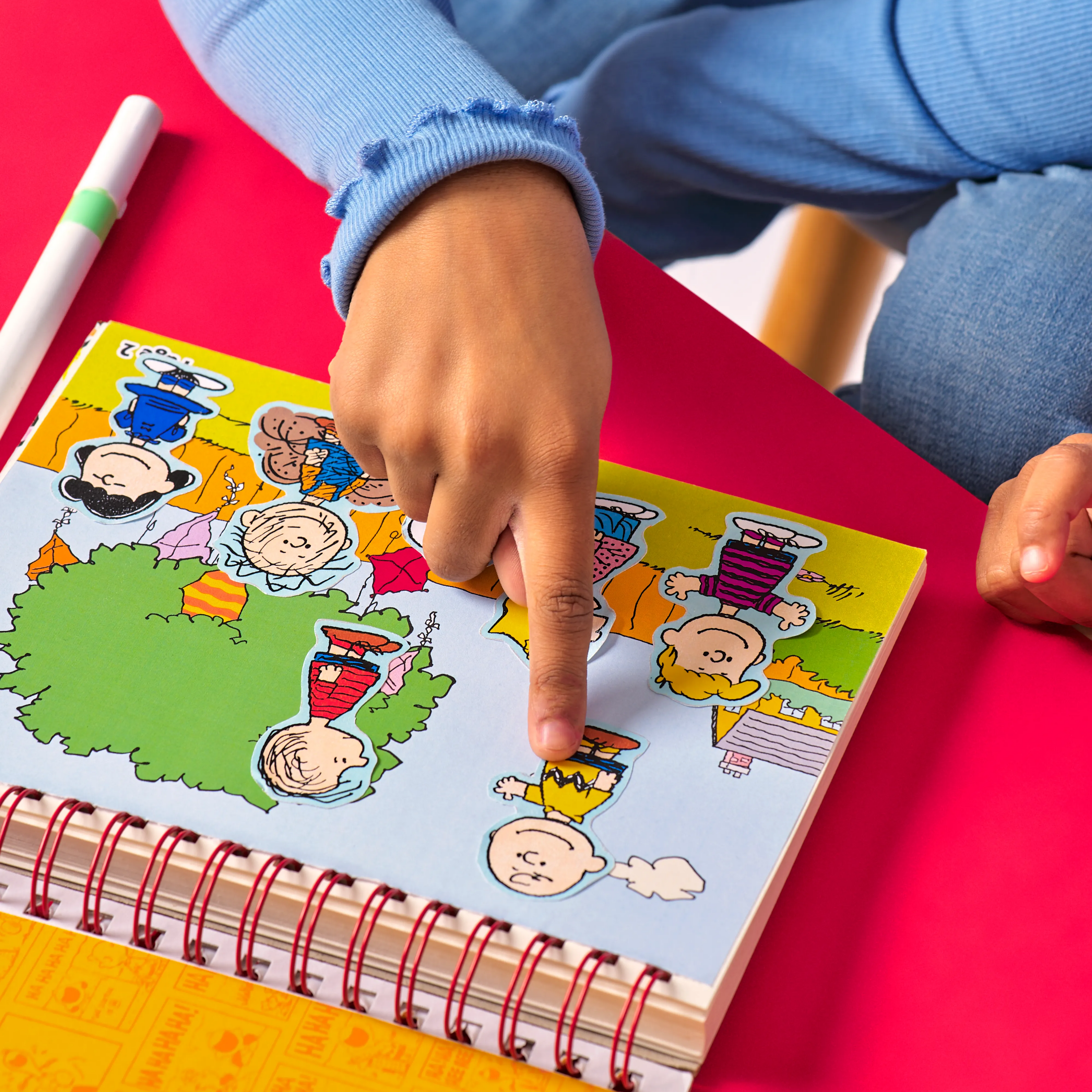 Kid applying Peanuts stickers in sticker page from the OOLY x Peanuts Coloring Activity & Sticker Kit