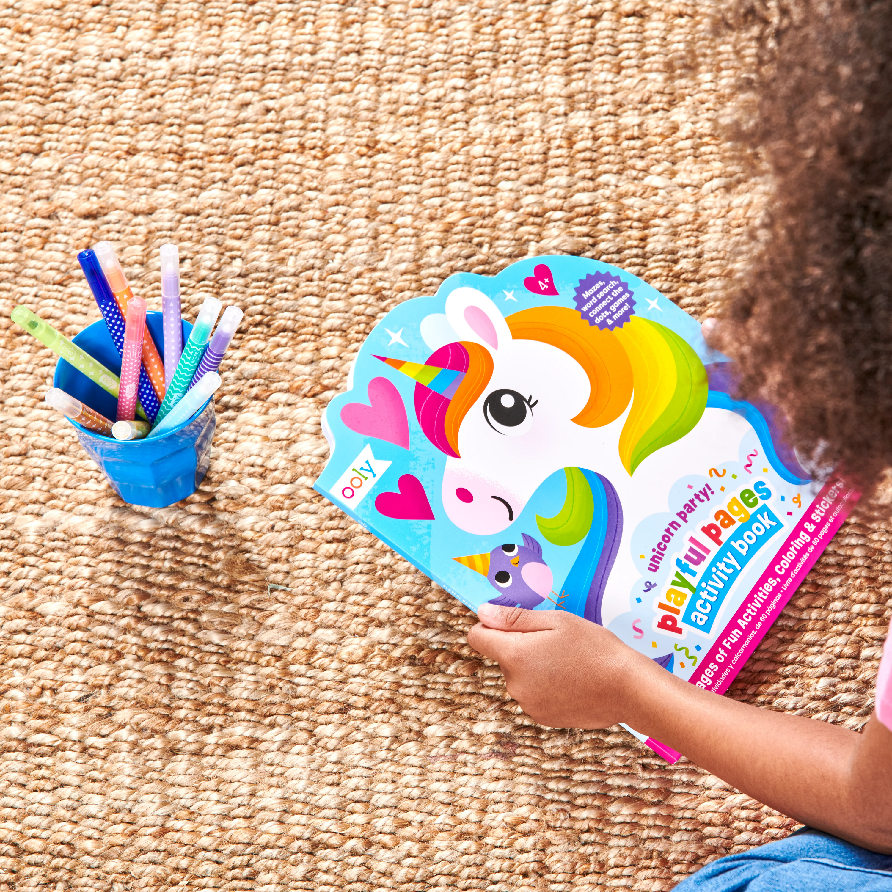 Girl looking at closed OOLY Playful Pages Activity Book - Games Coloring Stickers - Unicorn Party! activity book