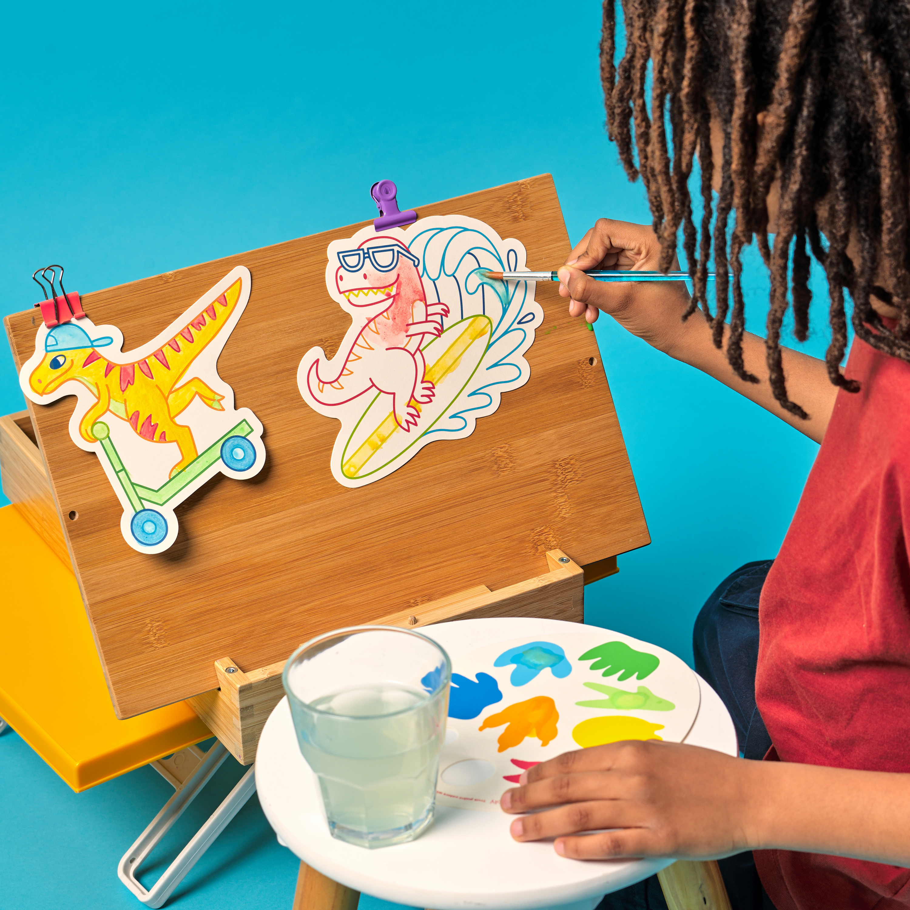 Kid painting a paint card from OOLY Chills and Thrills Dinos Playful Painters Easy Watercolor Painting Kit on a wooden easel