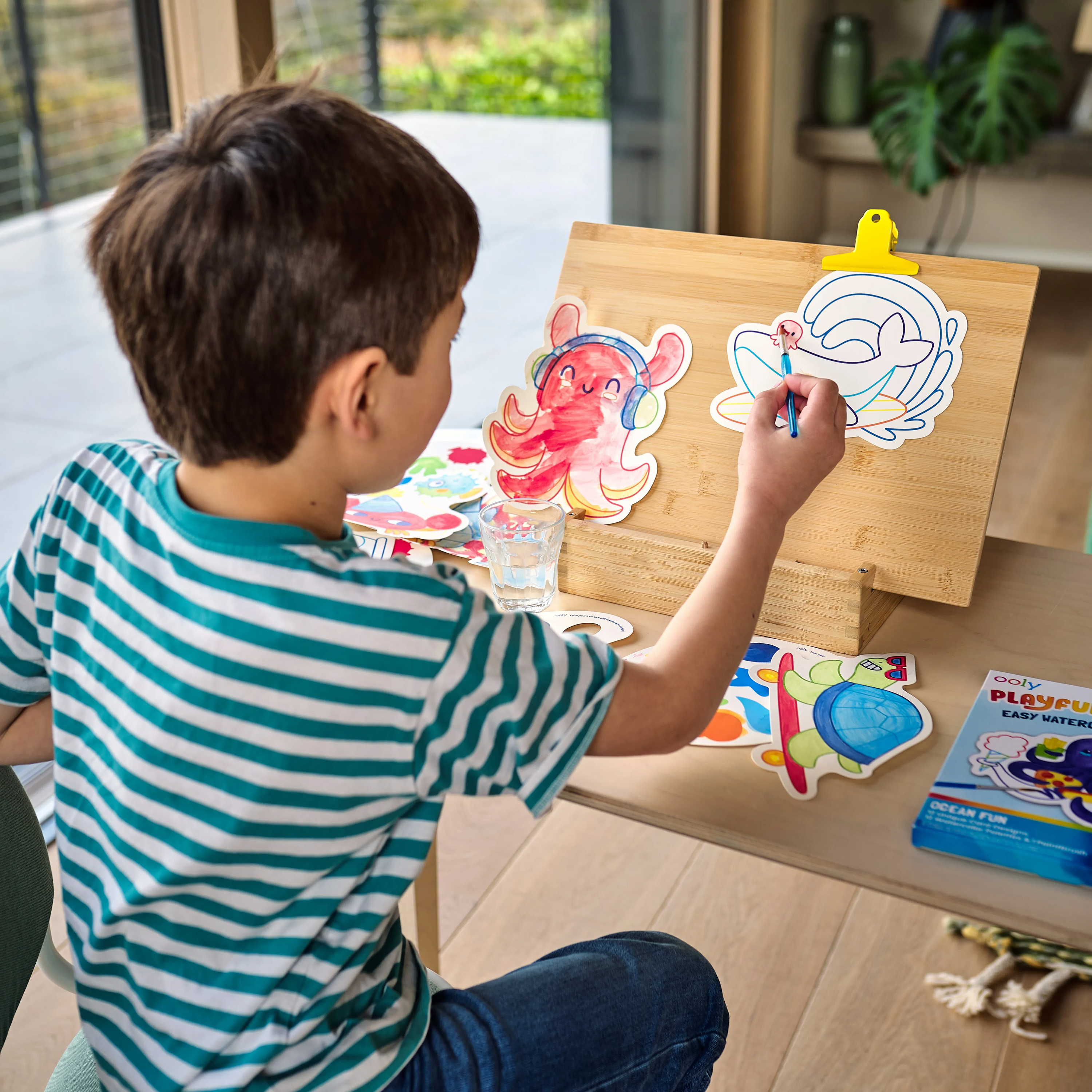 Kid painting watercolor paint cards from the OOLY Ocean Fun Playful Painters Easy Watercolor Painting Kit on a wooden easel