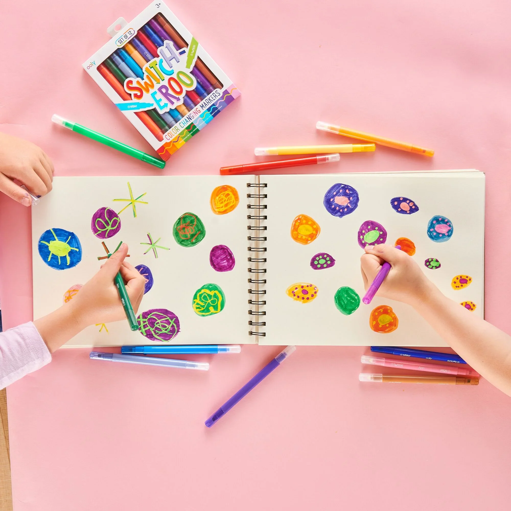 Two kids coloring in white notepad with OOLY Switch-Eroo markers on pink table