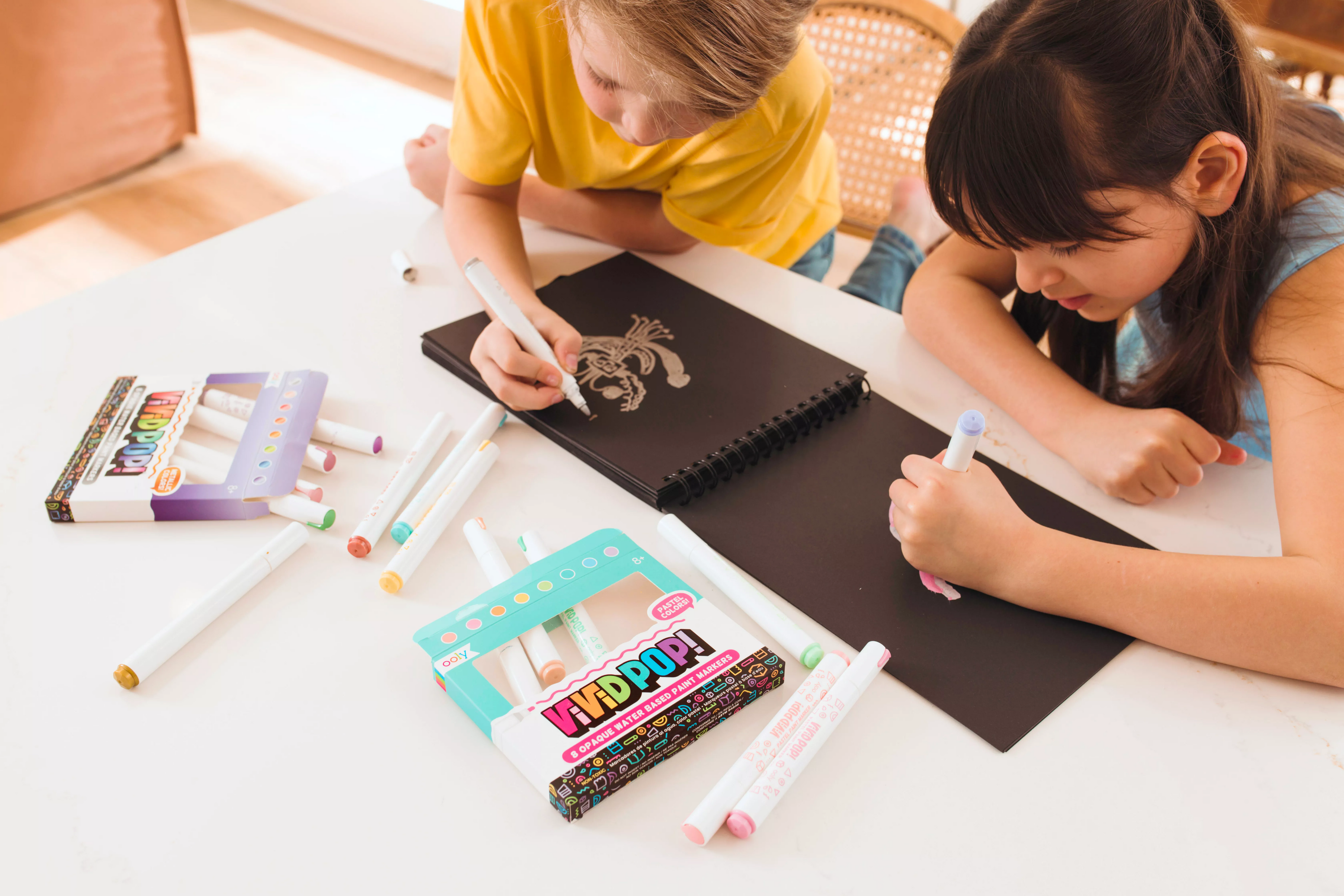 Two kids coloring on black paper pad with OOLY Vivid Pop! Paint Markers