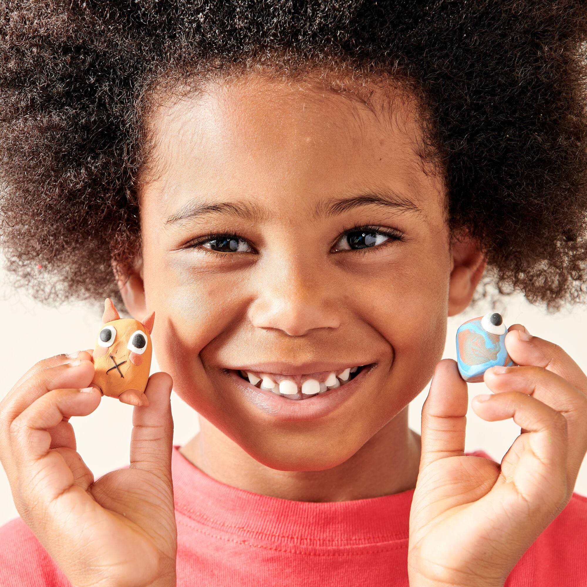 Kid holding two clay creations from a OOLY Creatibles Standard Air Dry Clay Kit
