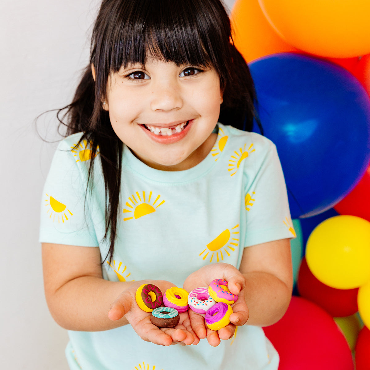 Happy girl standing in front of colorful balloons, holding dainty donuts erasers in her hands