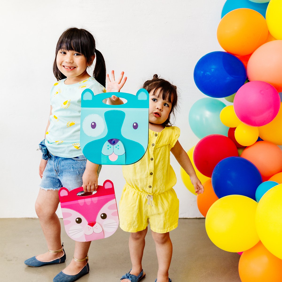 Happy girls holding dog and cat Carry Along Sketchbooks next to colorful balloons