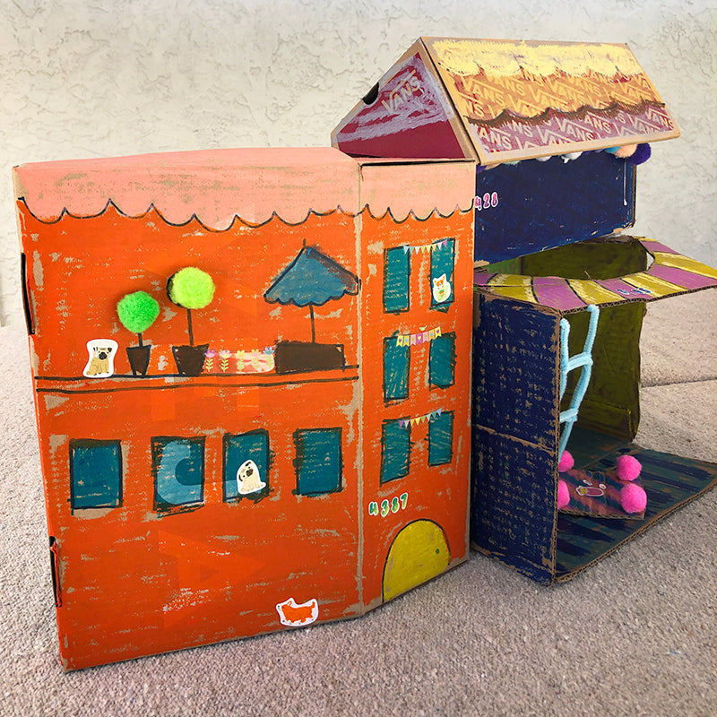 Cardboard boxes painted as a small town with buildings, windows, cat and dog stickers