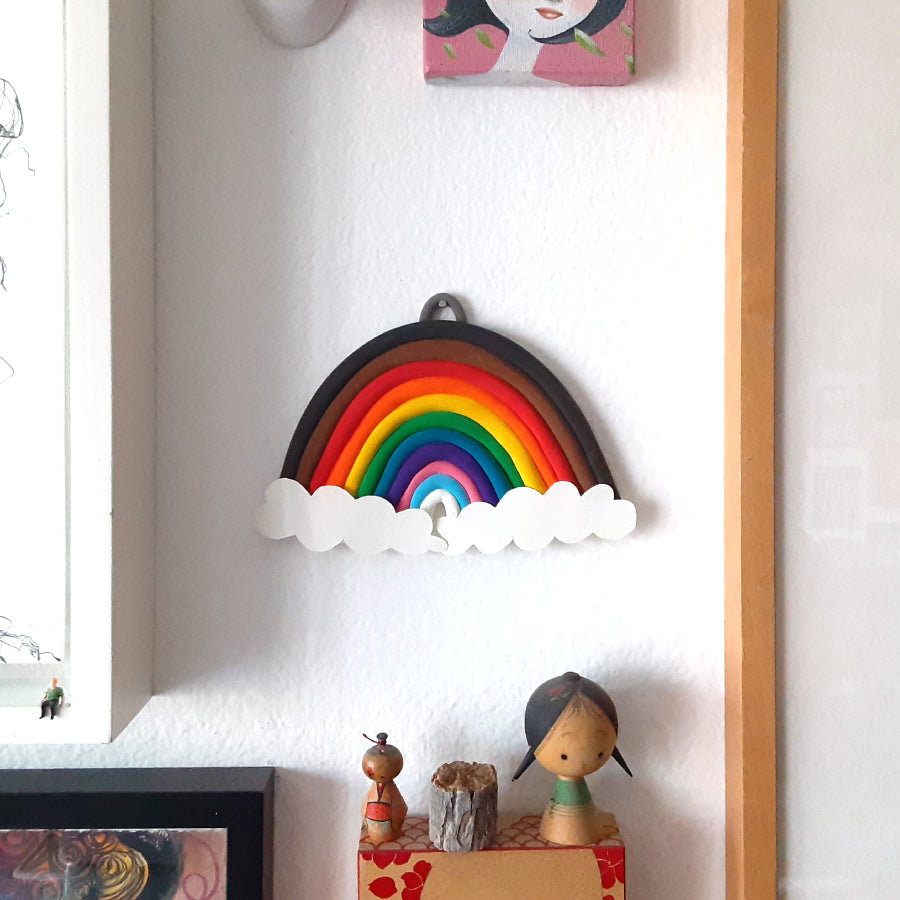 Clay rainbow with white paper clouds hanging on the wall next to other doll art and paintings