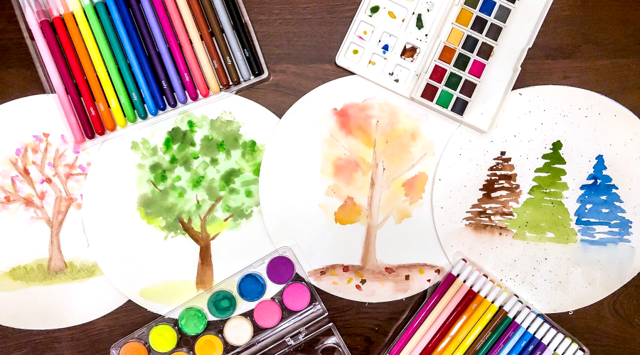 colorful watercolor trees on white circular paper with art supplies on brown surface