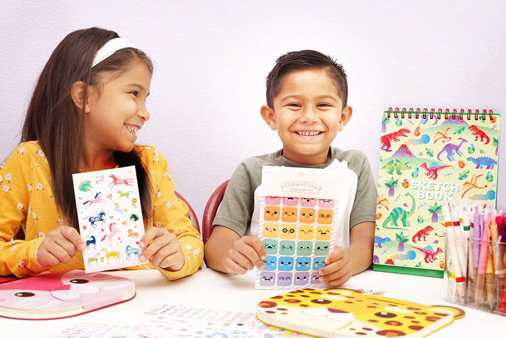 Boy and girl holding stickiville sticker pads and smiling with arts and crafts materials around them