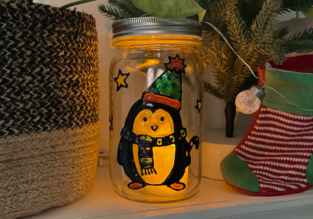 Penguin Creatibles DIY Window Cling Art on a mason jar in front of a candle with festive decor in the background