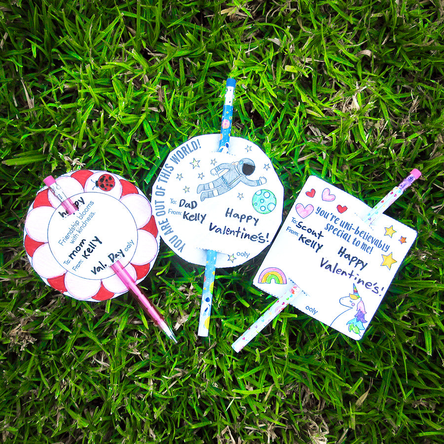 Three pencils with printable OOLY gift tags lying on green grass