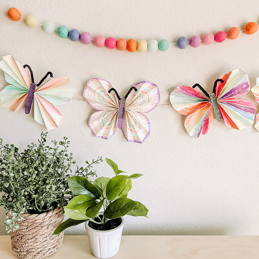Three Pastel Butterfly paper crafts hanging on the wall next to other decorations and plants
