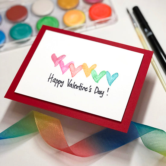Valentine's Day card next to a colorful ribbon and paints