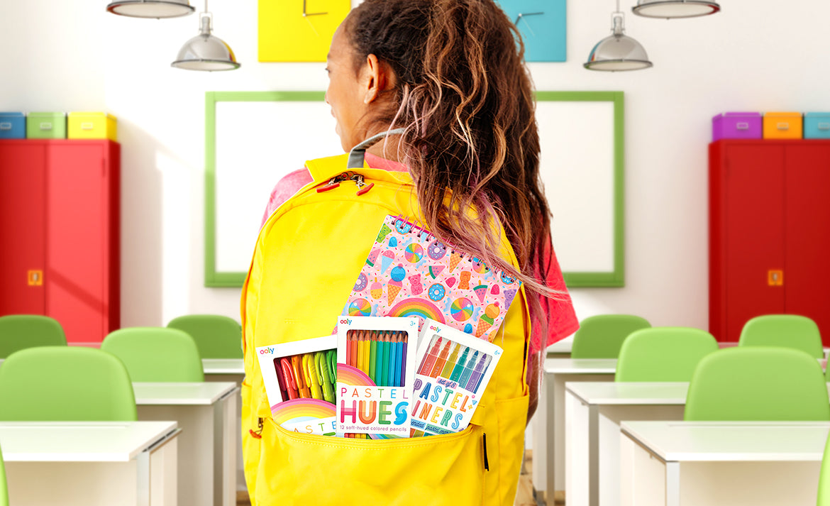 Girl with yellow backpack full of art supplies in a classroom with green chairs and red lockers