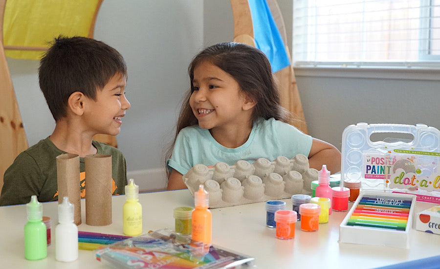 boy smiling at girl behind white table with craft supplies