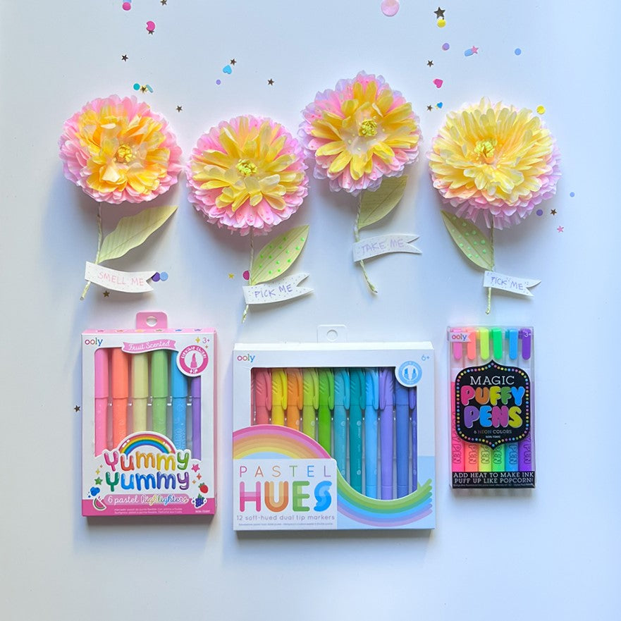 Colorful paper flowers with messages on the stems next to arts and crafts supplies