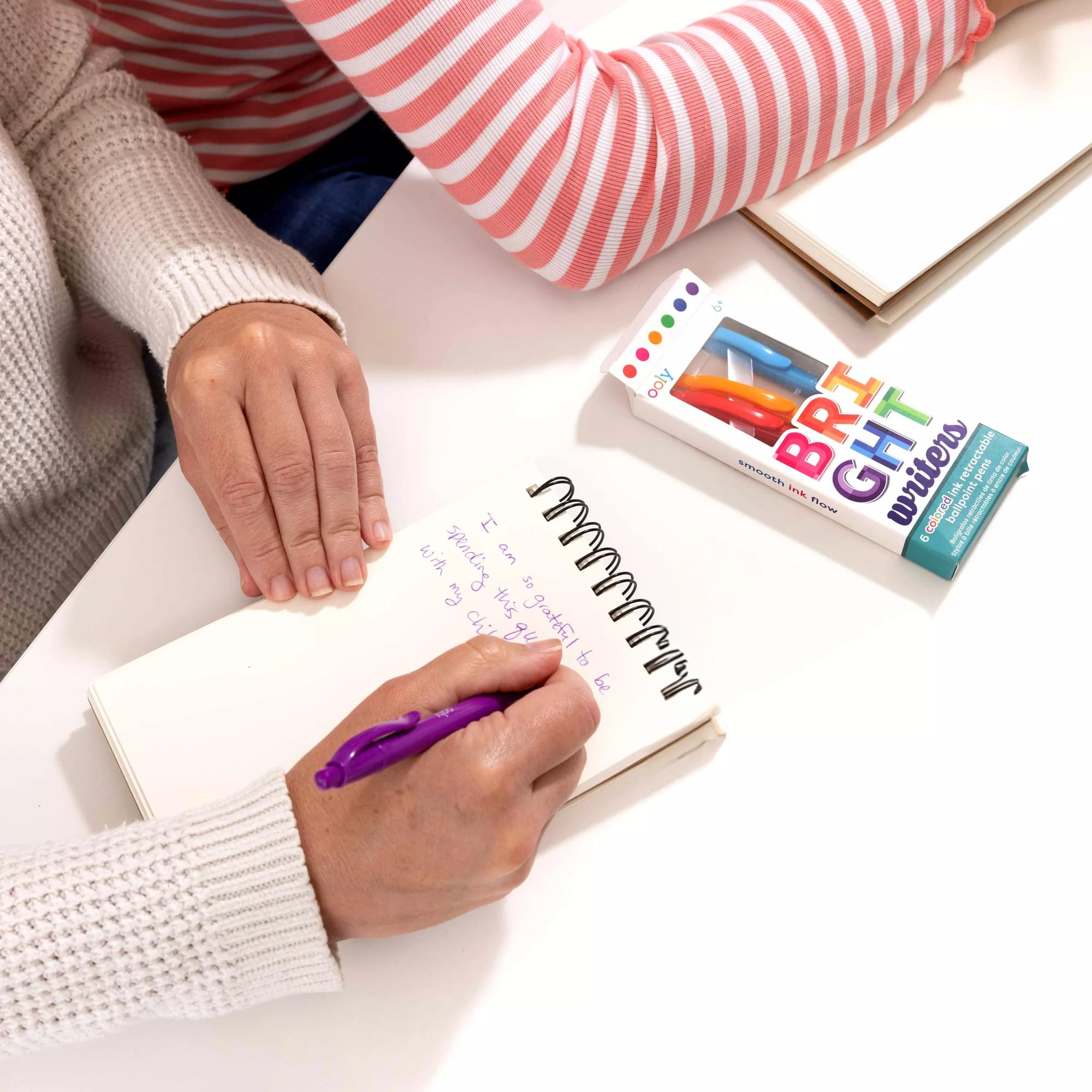Person writing on a notepad with OOLY Bright Writers Colored Ink Retractable Ballpoint Pens